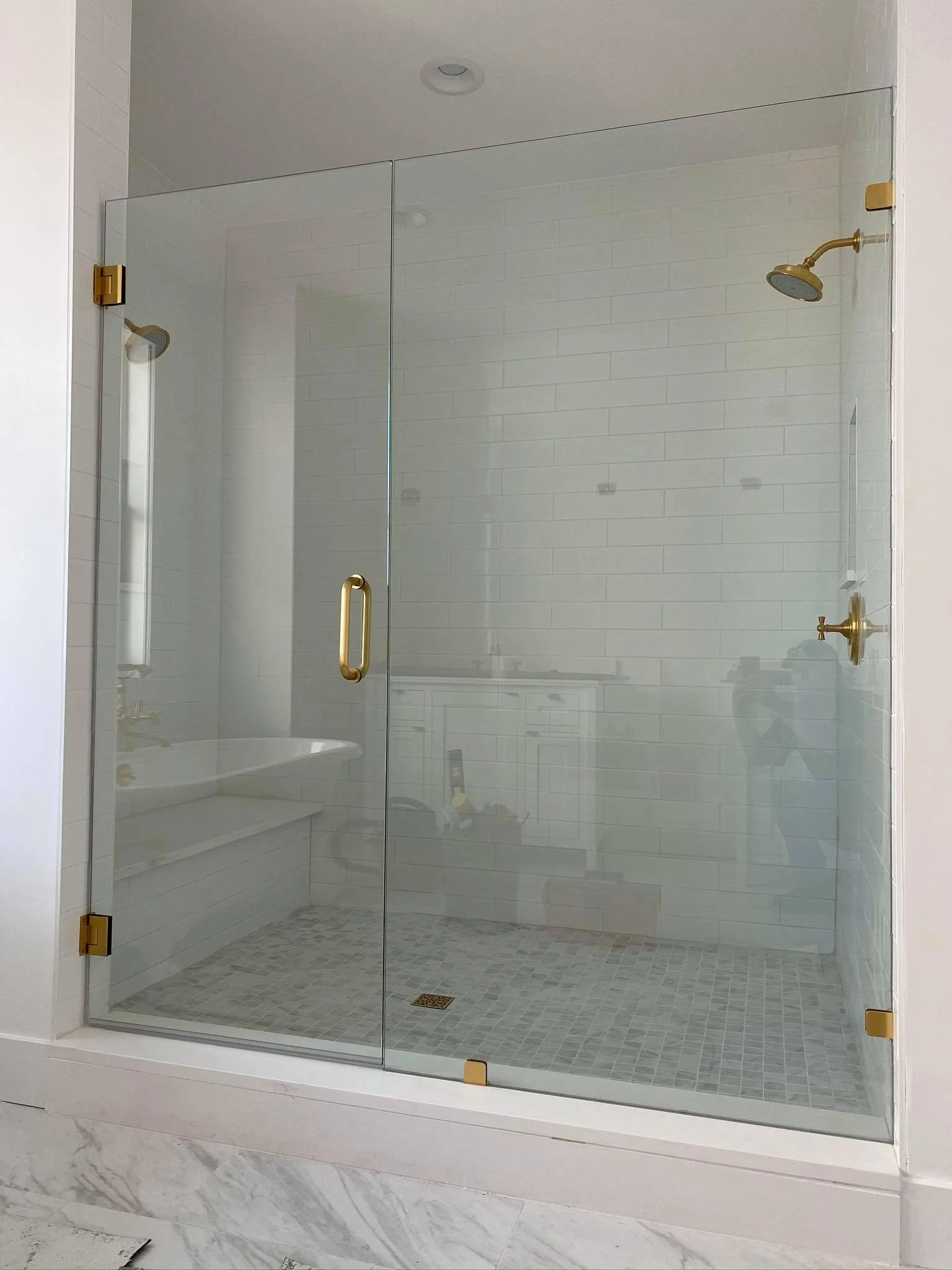 Empty glass-enclosed shower with white subway tiles, brass fixtures, and a mosaic tiled floor.