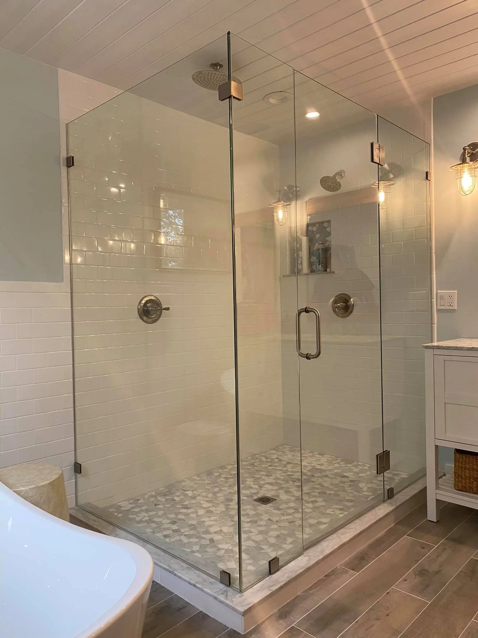 A modern walk-in shower with glass doors and tiled interior, featuring two showerheads and a niche for toiletries.