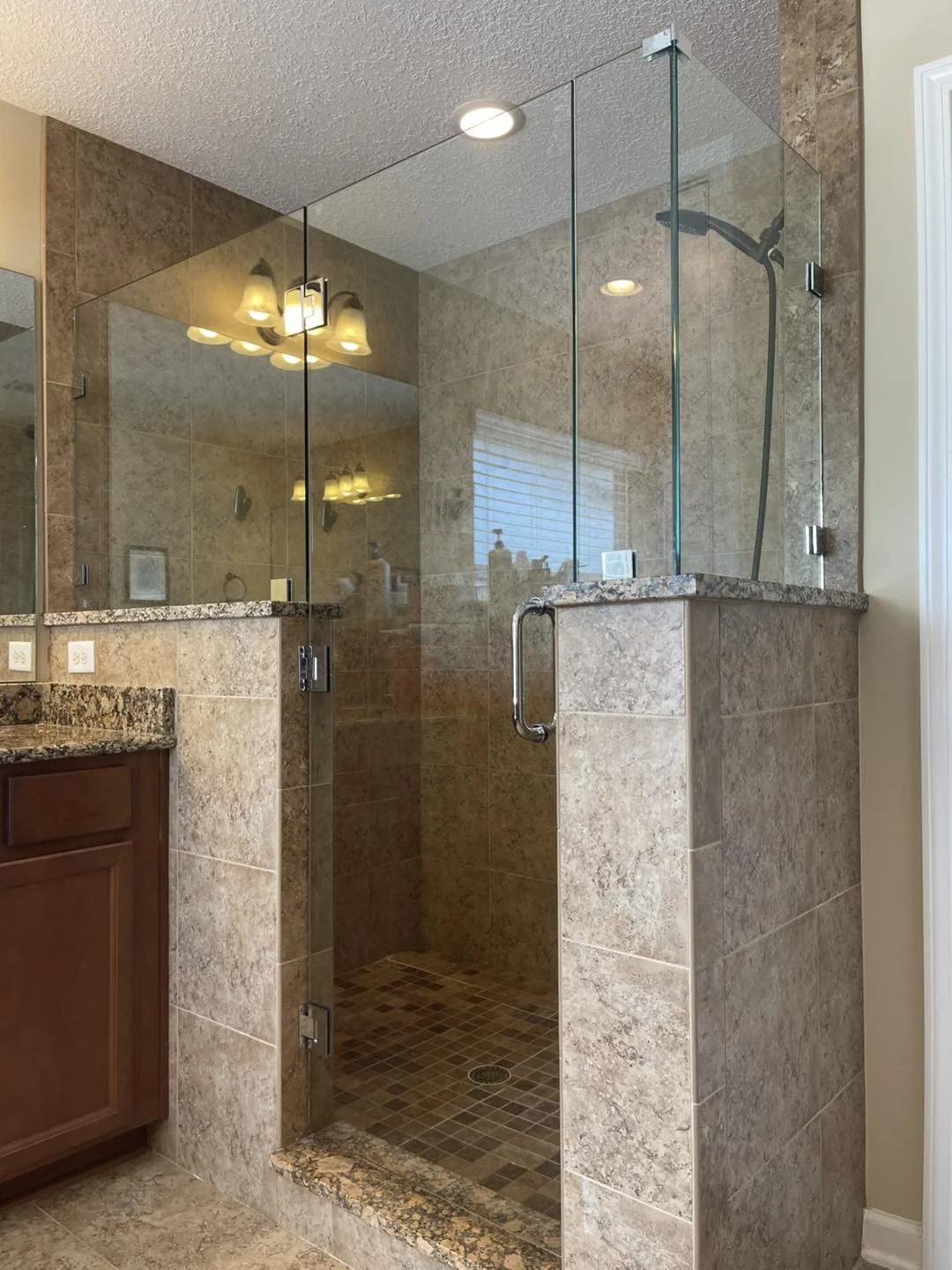 A glass-enclosed shower with brown tiled walls and a mosaic tiled floor in a bathroom. The shower has a built-in ledge and a black showerhead.