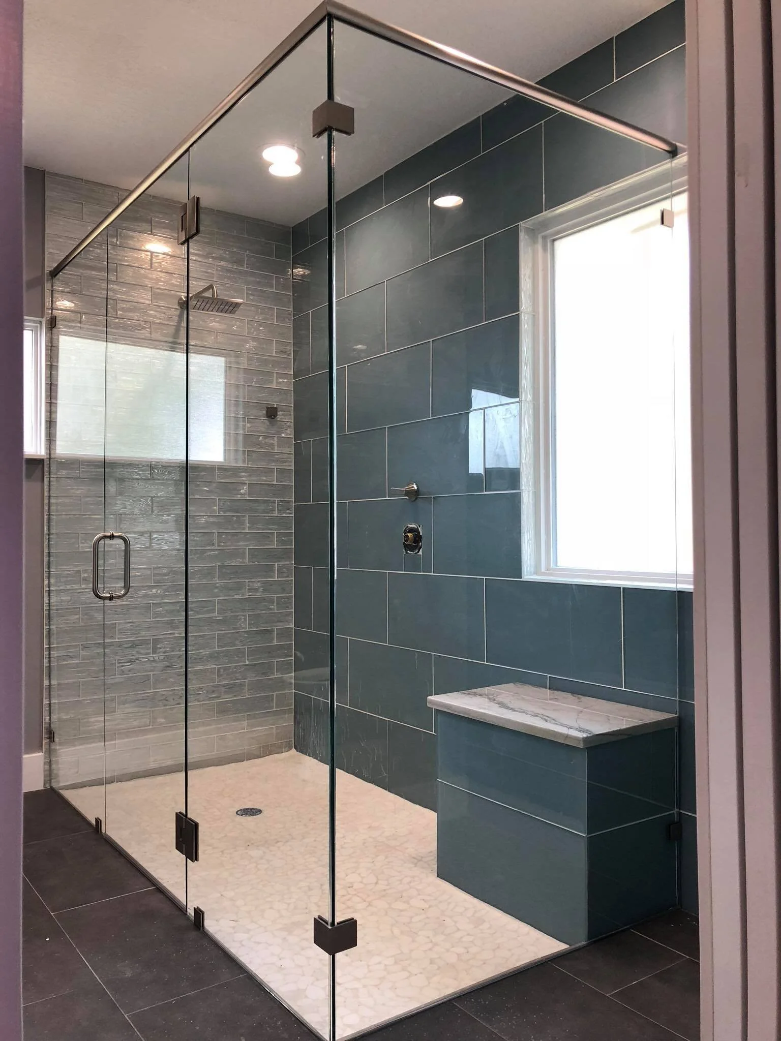 Modern glass-enclosed shower with gray tile walls, a window, and a built-in bench.