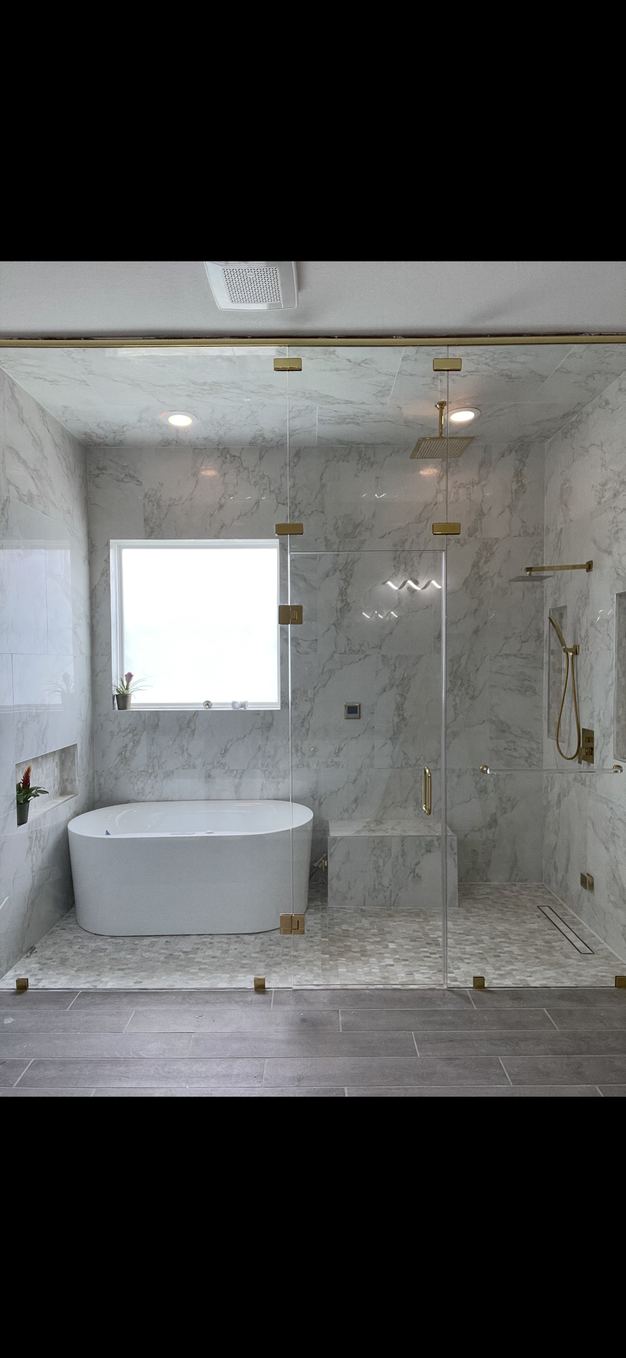 Bathroom with a glass shower enclosure, wooden cabinetry, a blue countertop, a towels on a towel bar, vases on the floor, and a white rug in front of the shower.