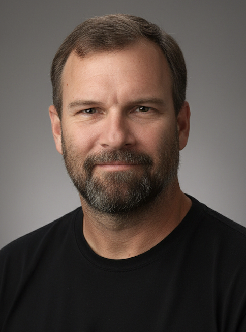 A middle-aged man with brown hair and a beard, wearing a black shirt, looking at the camera against a gray background.