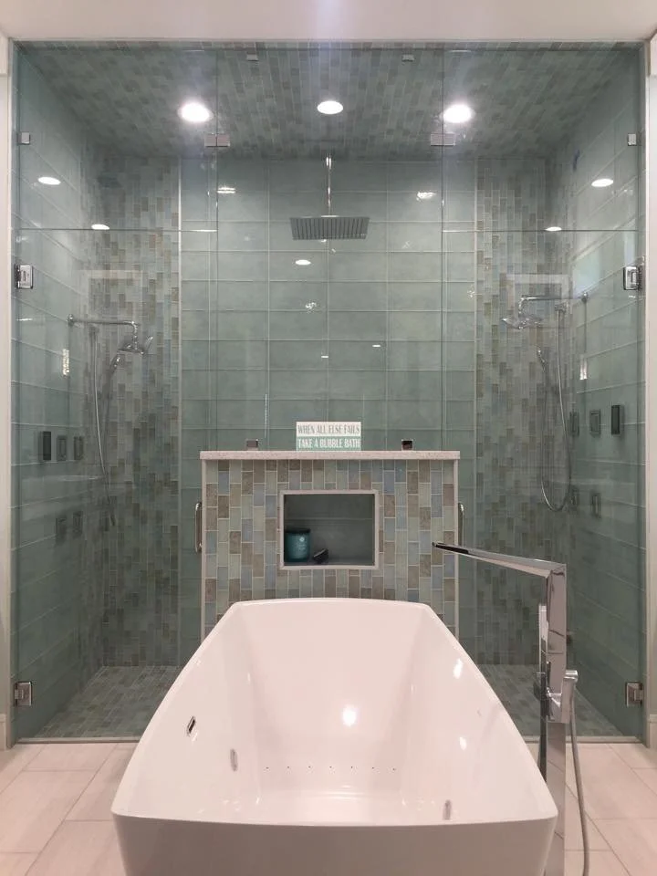Modern bathroom with a bathtub in front of a glass-enclosed shower area featuring multiple shower heads and a niche with a sign that reads 'When all else fails, take a bubble bath.'