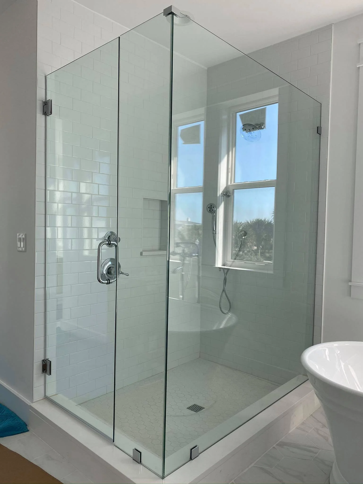 Modern glass shower enclosure with white subway tile walls, shower head, and a small window.