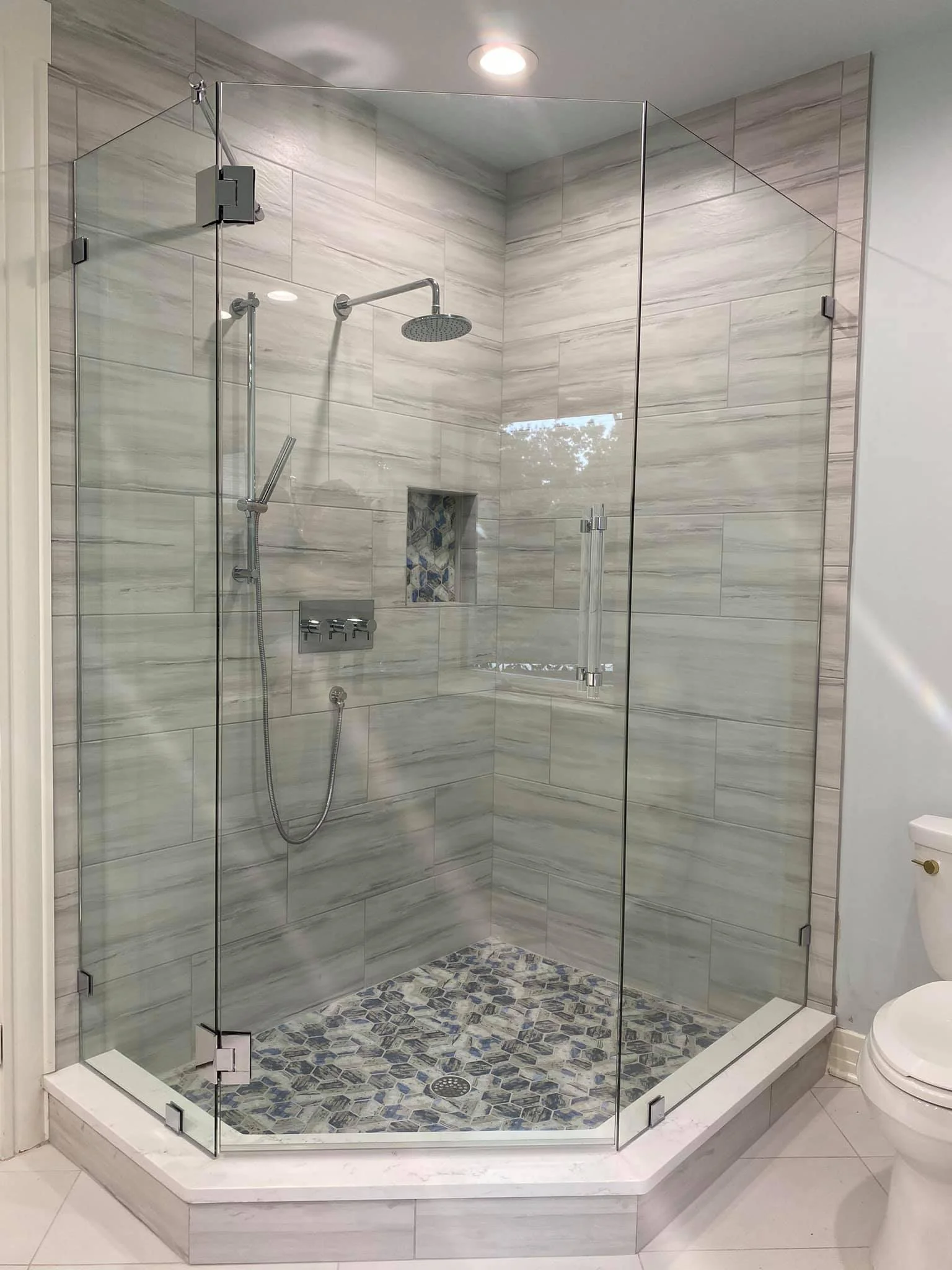 A modern glass shower enclosure with marble tiles, a built-in niche, and pebble stone shower floor in a bathroom.