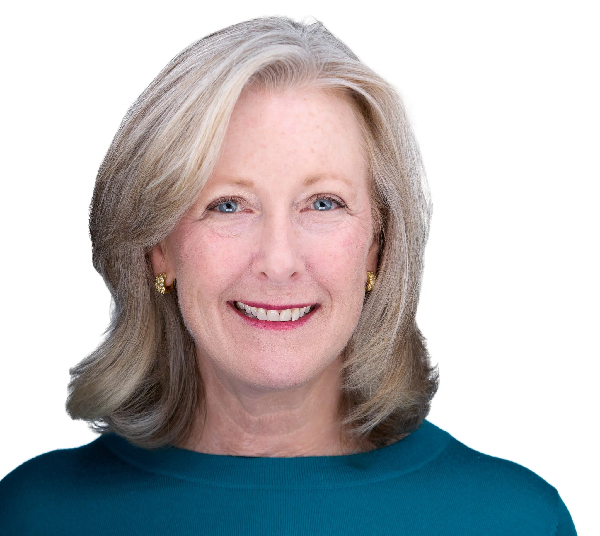 A smiling middle-aged woman with blonde hair, blue eyes, wearing a teal top and gold earrings.