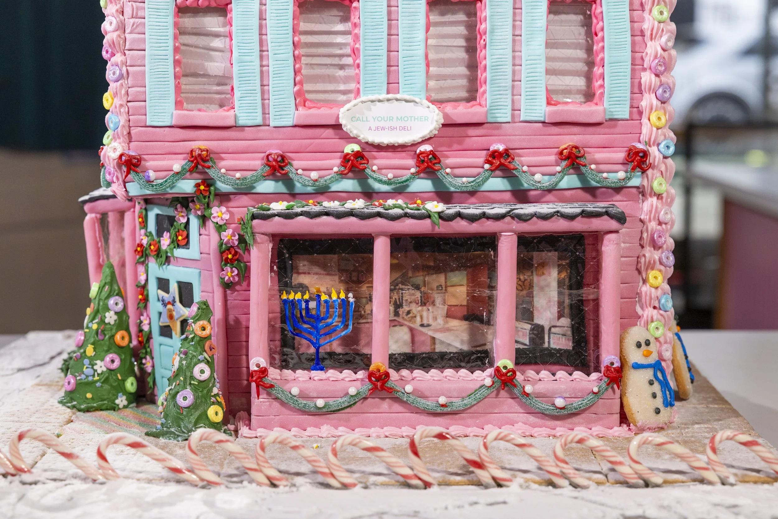 Decorated gingerbread house with pink icing, Christmas trees, candy canes, and snowman cookies.