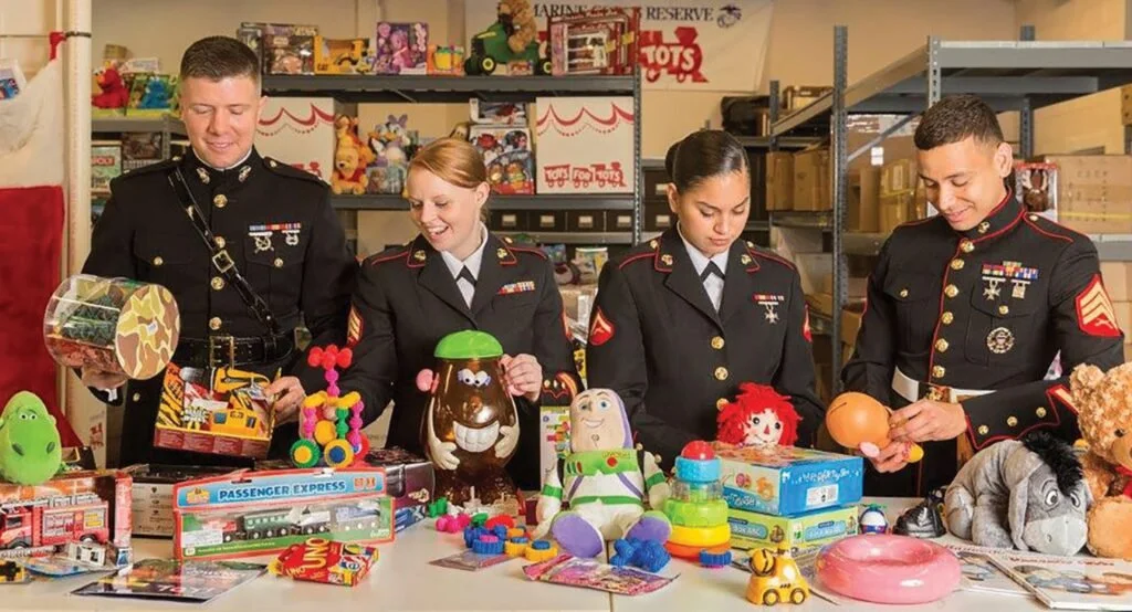 Four people in military uniforms browsing toy trees, stuffed animals, and amusement park toys on a table at a toy store.