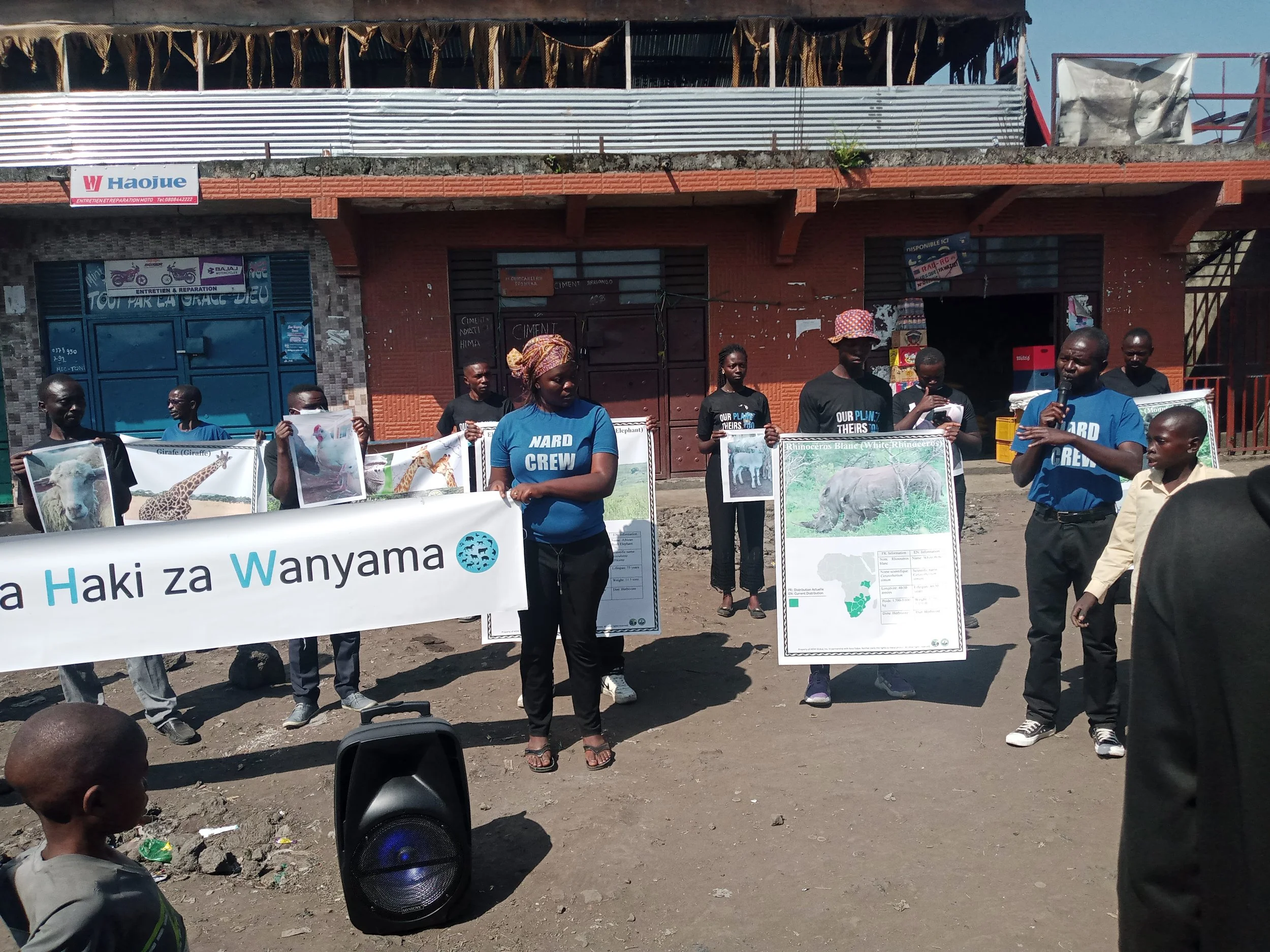 Group of people holding posters and banner about wildlife conservation in an outdoor setting, with small children watching.