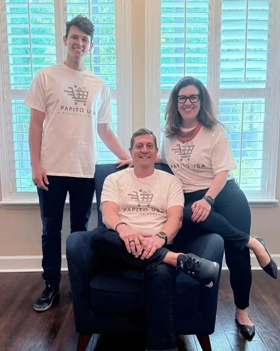 Três pessoas em uma sala com janelas com venezianas brancas ao fundo, vestindo camisetas brancas com o logo e nome do Partido Republican USA, uma mulher e dois homens. A mulher está apoiando um homem sentado em uma cadeira, enquanto outro homem está ao lado deles.