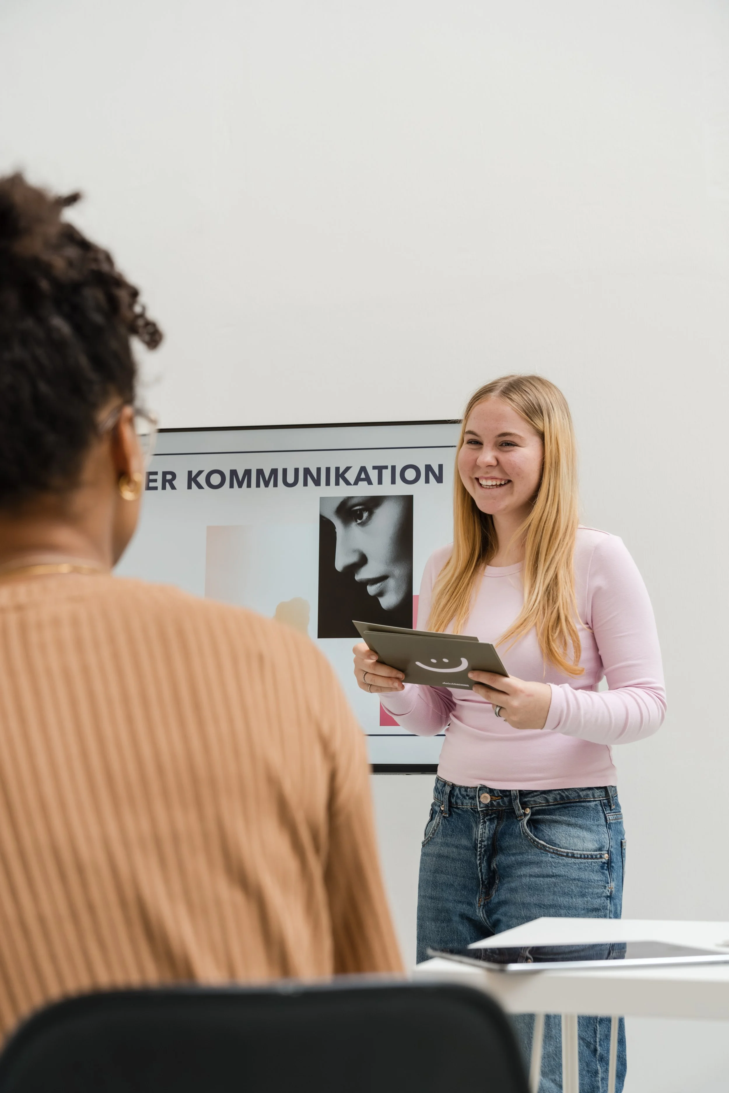 Eine junge Frau präsentiert eine Präsentation vor einer Gruppe während eines Kurses oder einer Schulung in einem modernen Classroom mit Whiteboard im Hintergrund.