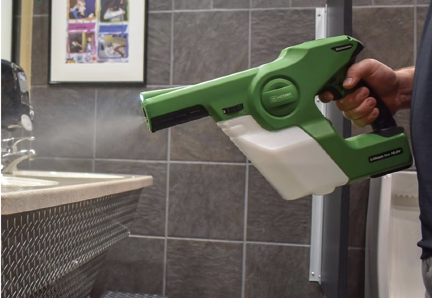 Person holding a green and white handheld steam cleaner in a room with gray tiled walls.