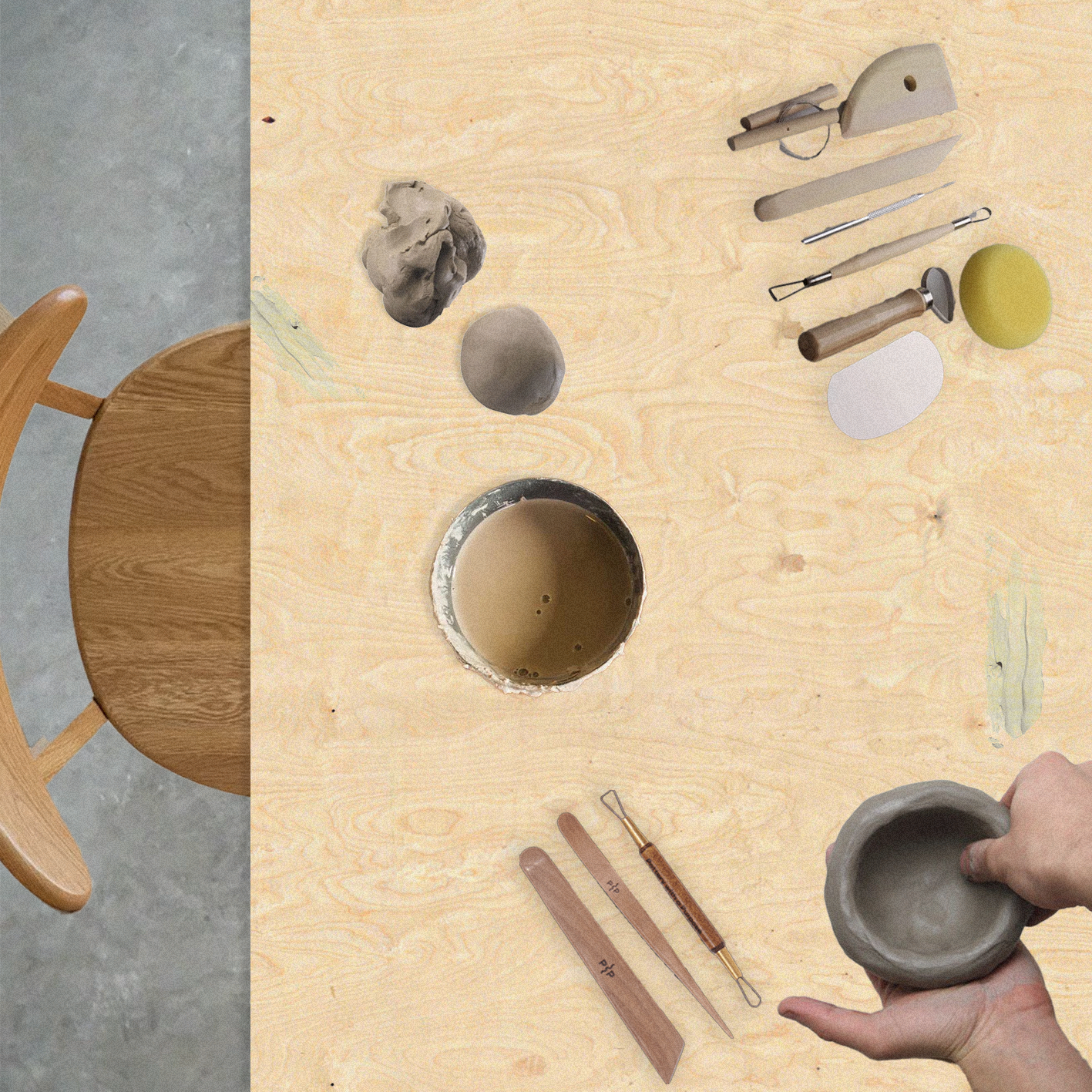 Top-down view of a wooden table with pottery tools, a cup of water, and a person's hands shaping a pottery piece. Part of a wooden chair is visible at the edge of the table.