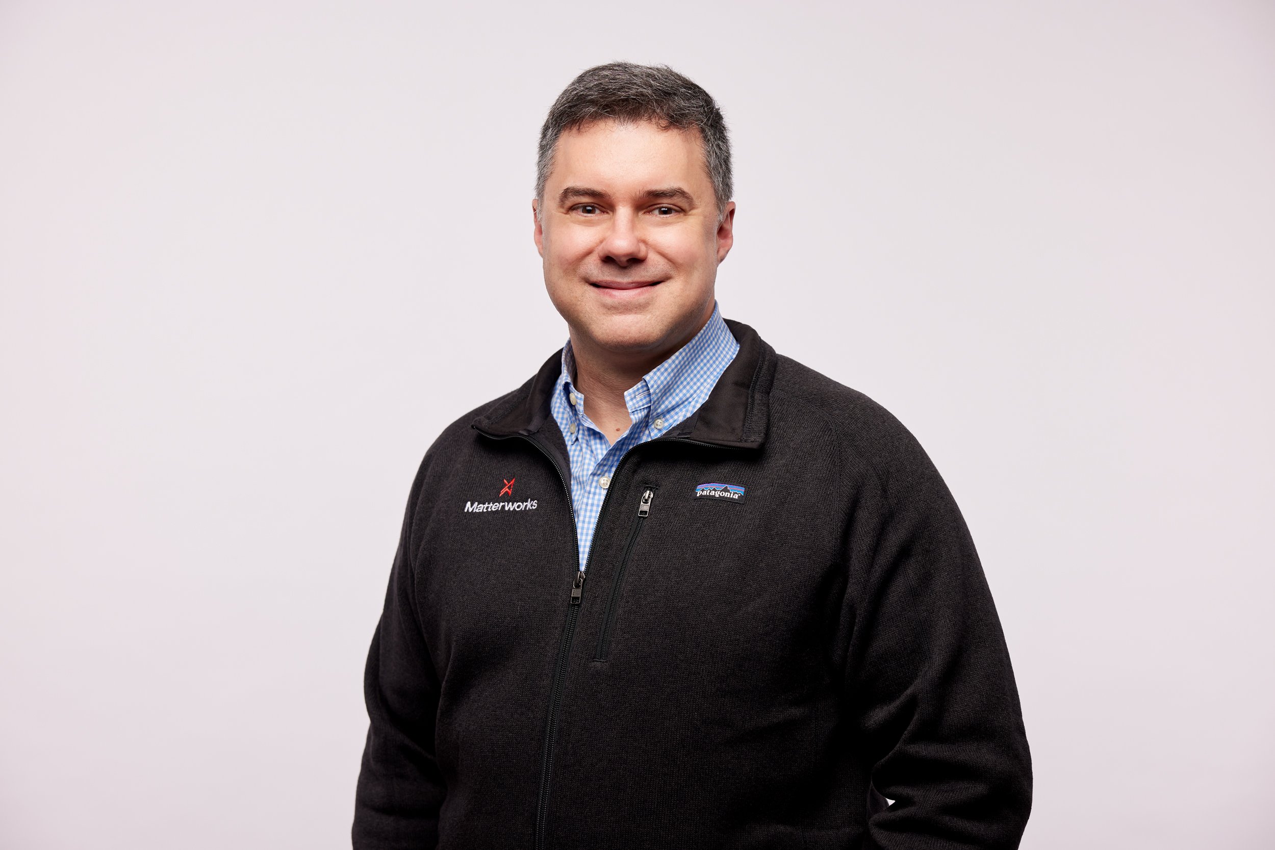 A man smiling, wearing a black Patagonia jacket with Matterworks logo, standing against a plain white background.