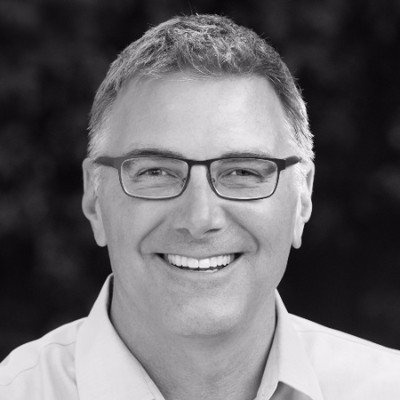 Black and white photo of a smiling man with glasses, short hair, and a collared shirt.