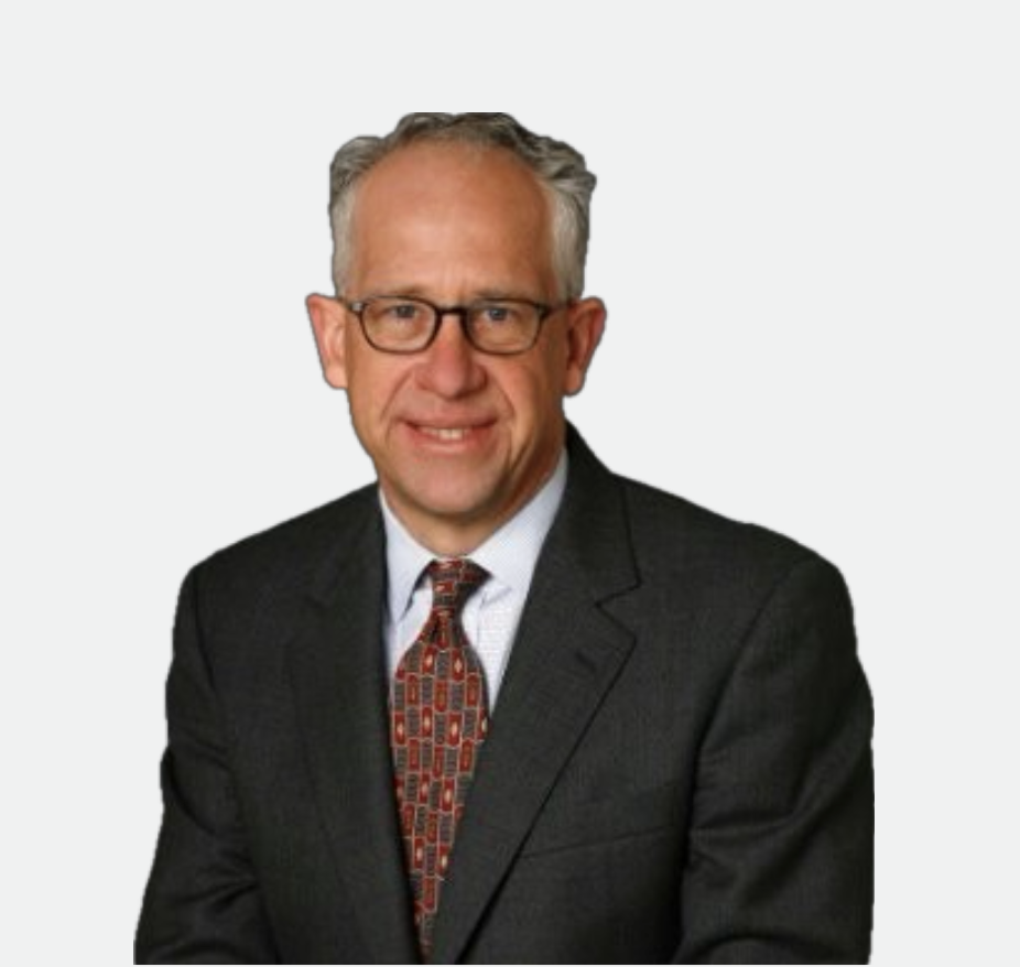 A middle-aged man with gray hair and glasses wearing a dark suit, white shirt, and patterned tie, smiling at the camera.