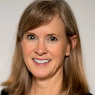 Close-up of a smiling woman with shoulder-length light brown hair and blue eyes.
