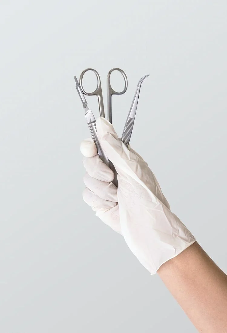 Mano con guanto bianco che tiene strumenti chirurgici: forbici, pinzette e bisturi
