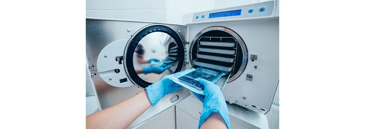 Operatore sanitario inserisce un sacchetto di plastica nel lavatrice sterilizzatrice automatica in un ambiente clinico.