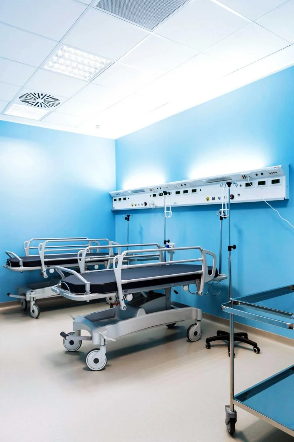 Stanza di ospedale con letti, apparecchiature mediche e pareti azzurri.