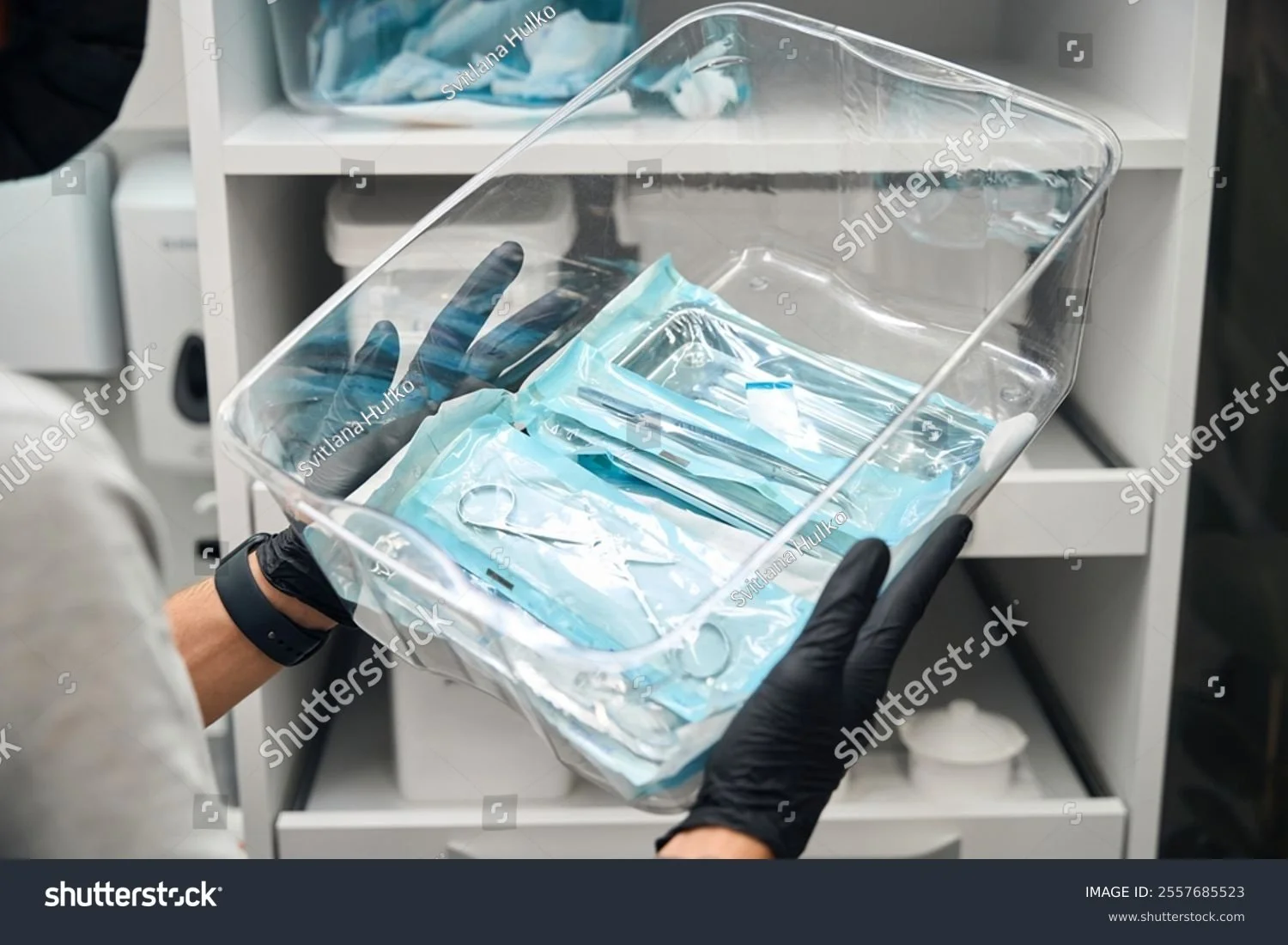 Una persona con guanti neri tiene in mano un contenitore di plastica con sacchetti di siero e attrezzature mediche sterili, all'interno di un'apparecchiatura medica.