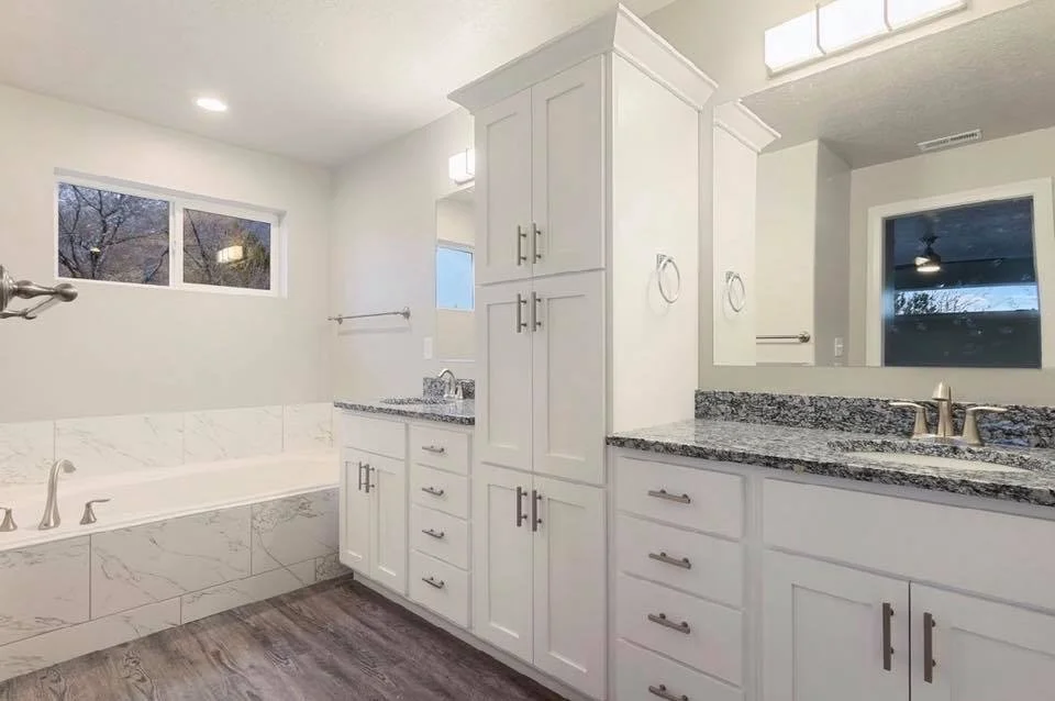 Bathroom with a large bathtub, granite countertops, white cabinets, and a window showing trees outside.