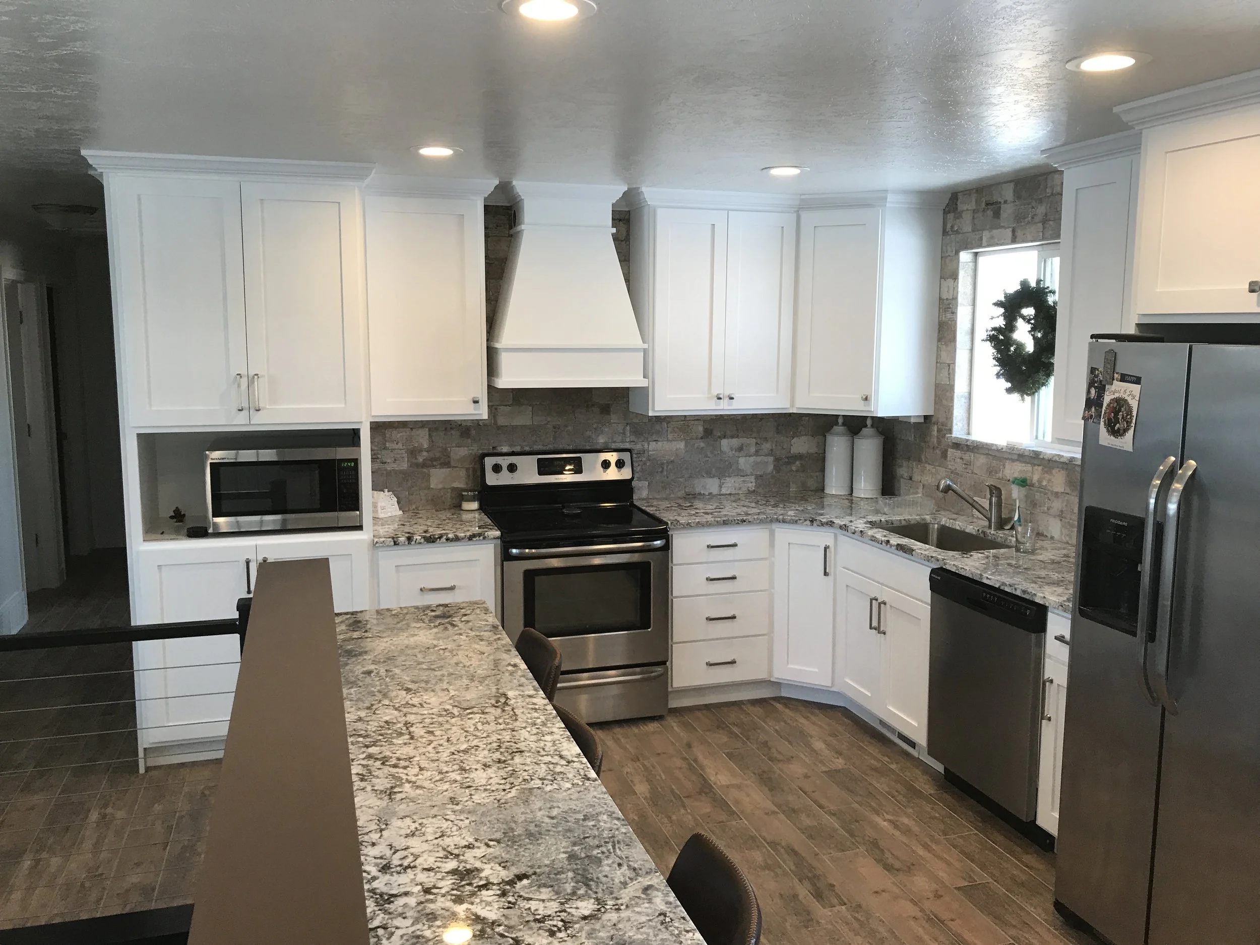 Modern kitchen with white cabinets, stainless steel appliances, granite countertops, brick backsplash, and hardwood flooring. Includes microwave, oven, refrigerator, and sink with window above.