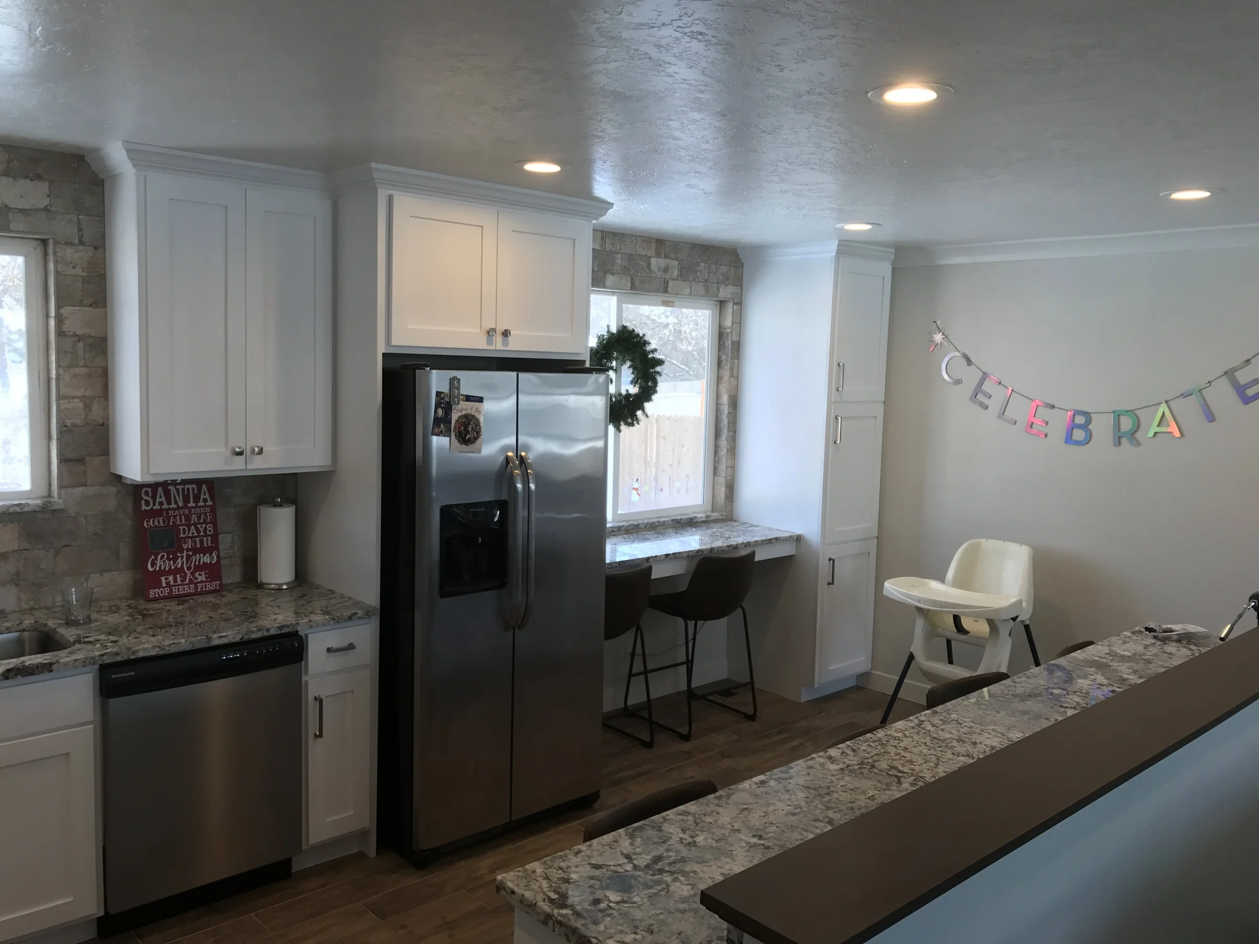 Bright kitchen with white cabinets, granite countertops, a stainless steel refrigerator, and a decorated wall with a colorful 'Celebrate' banner for a celebration.