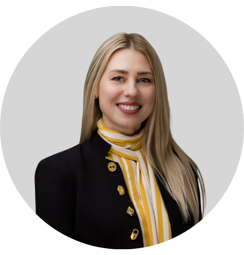 A woman in a black blazer with gold buttons and a yellow and white striped scarf, smiling at the camera.