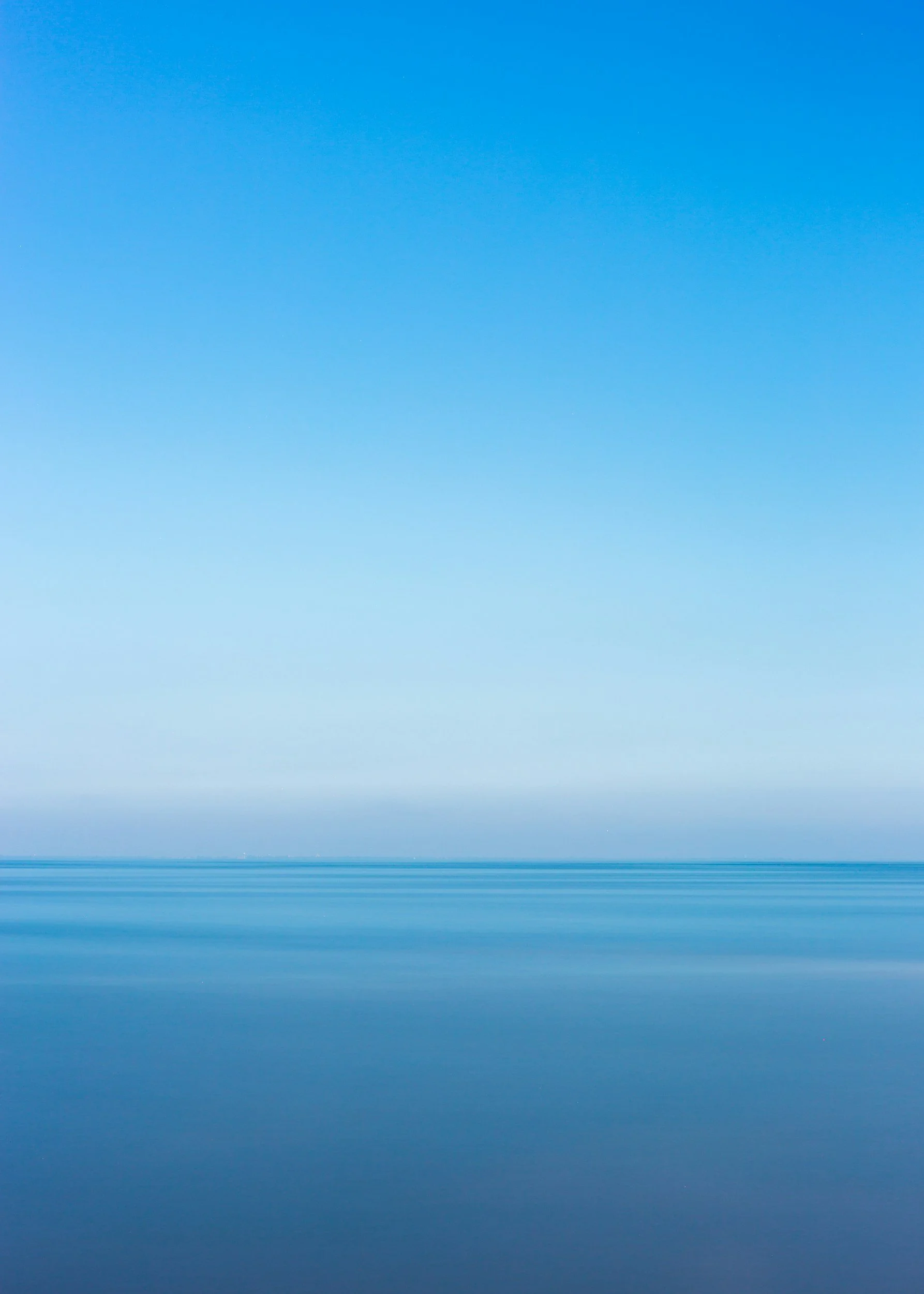 A calm body of water reflecting a clear, blue sky with minimal cloud cover.