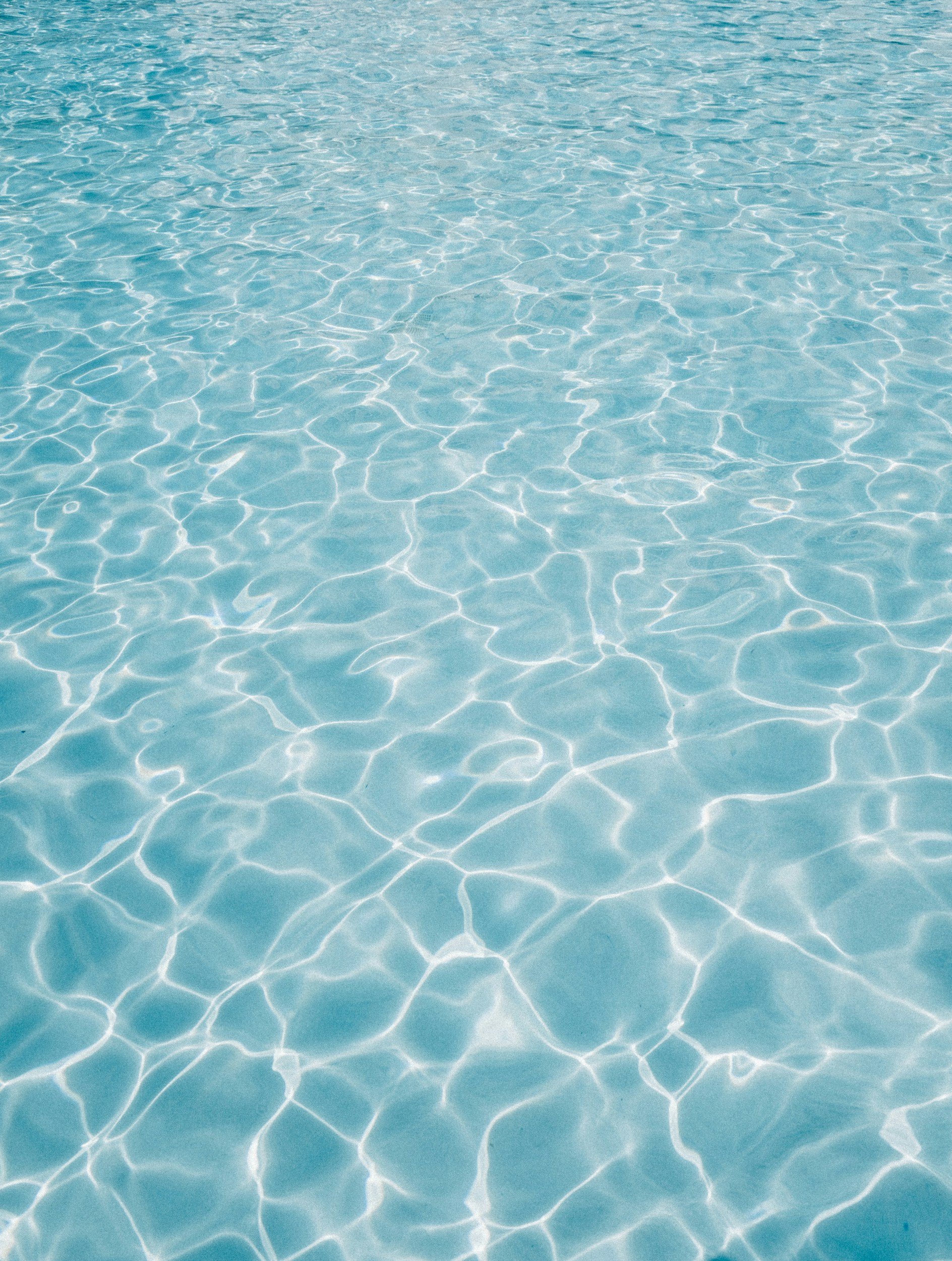 A clear swimming pool with sunlight reflections on the water's surface.