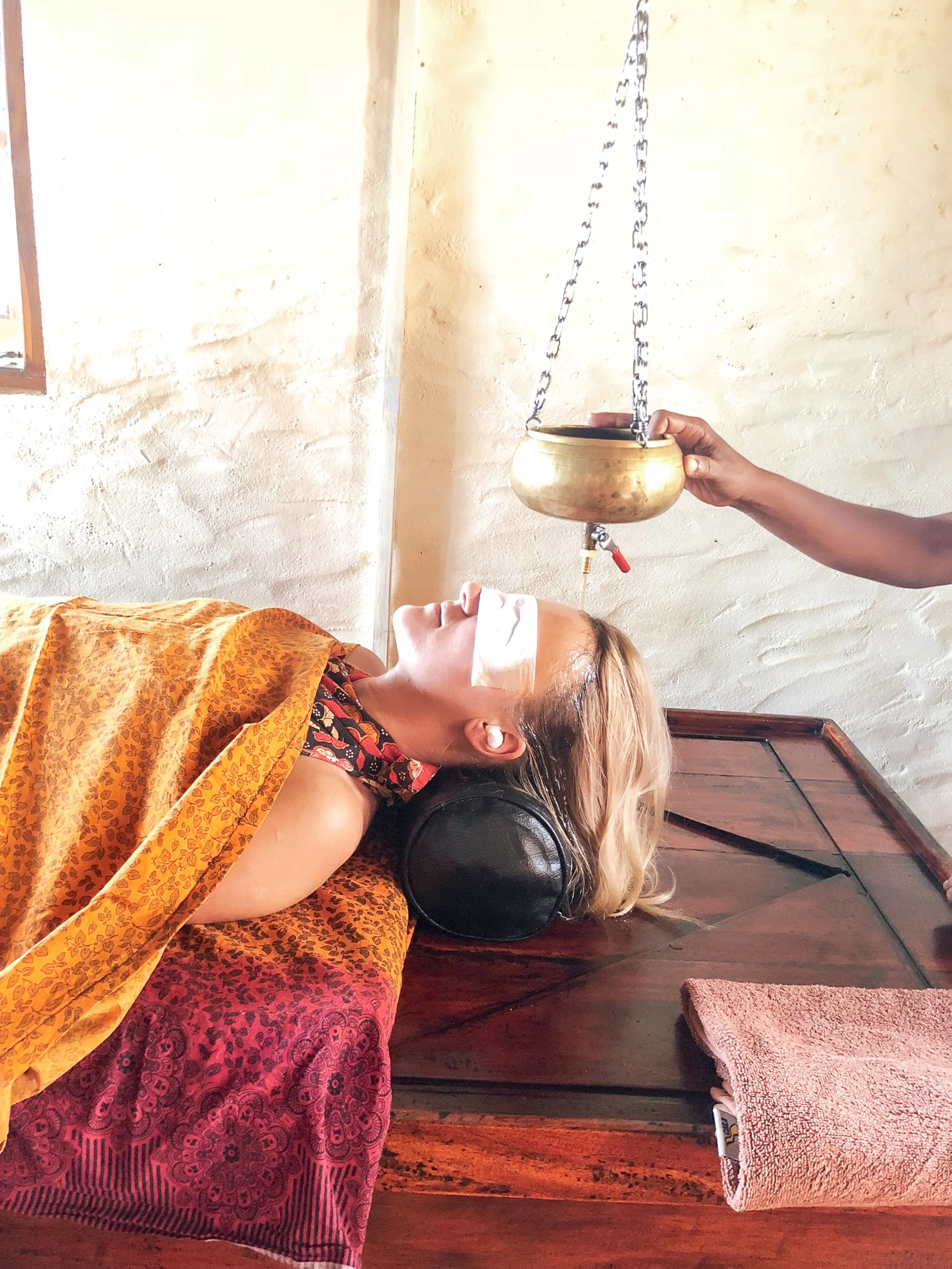 Žena leží se zavřenýma očima a přijímá léčebnou ájurvédskou terapii s visící mosaznou mísou v Isolabella Ayurveda Resort.