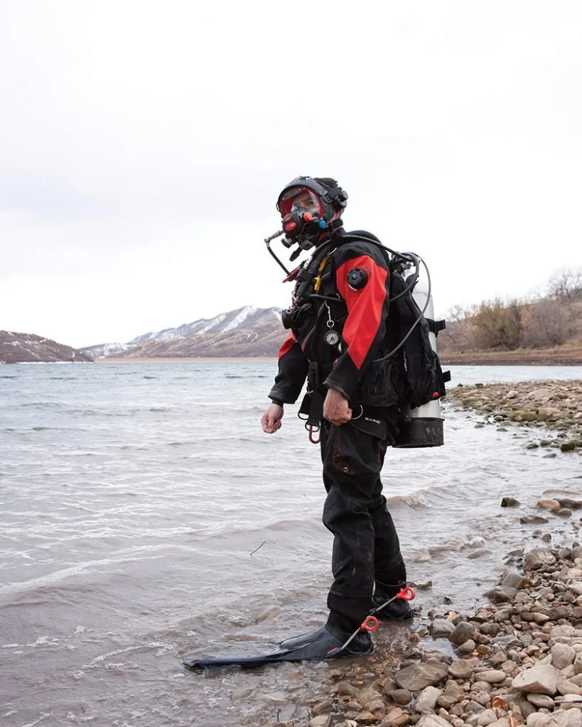 Search and rescue diver in scuba equipment beside a mountain lake.