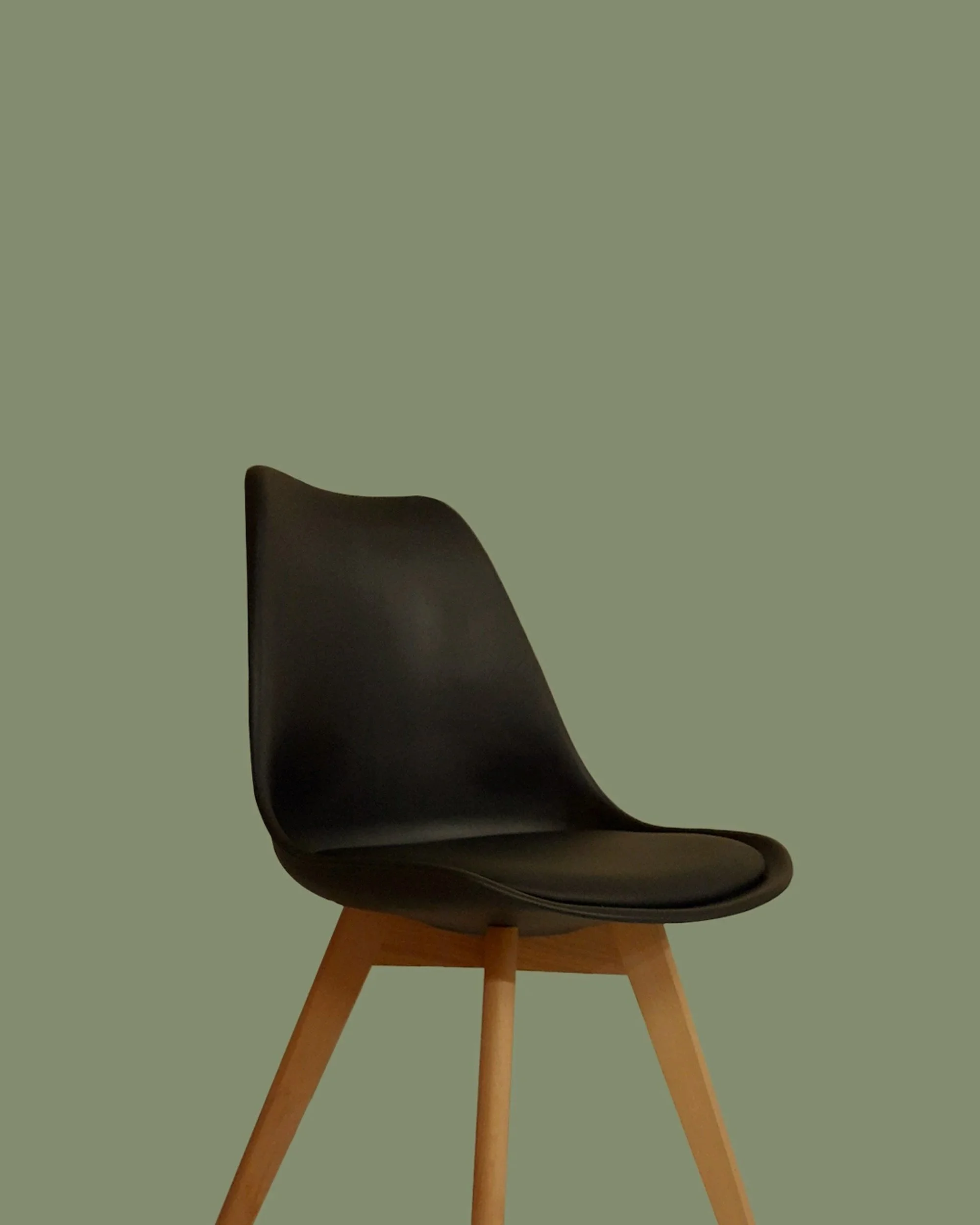 A modern black chair with wooden legs against a muted green background.