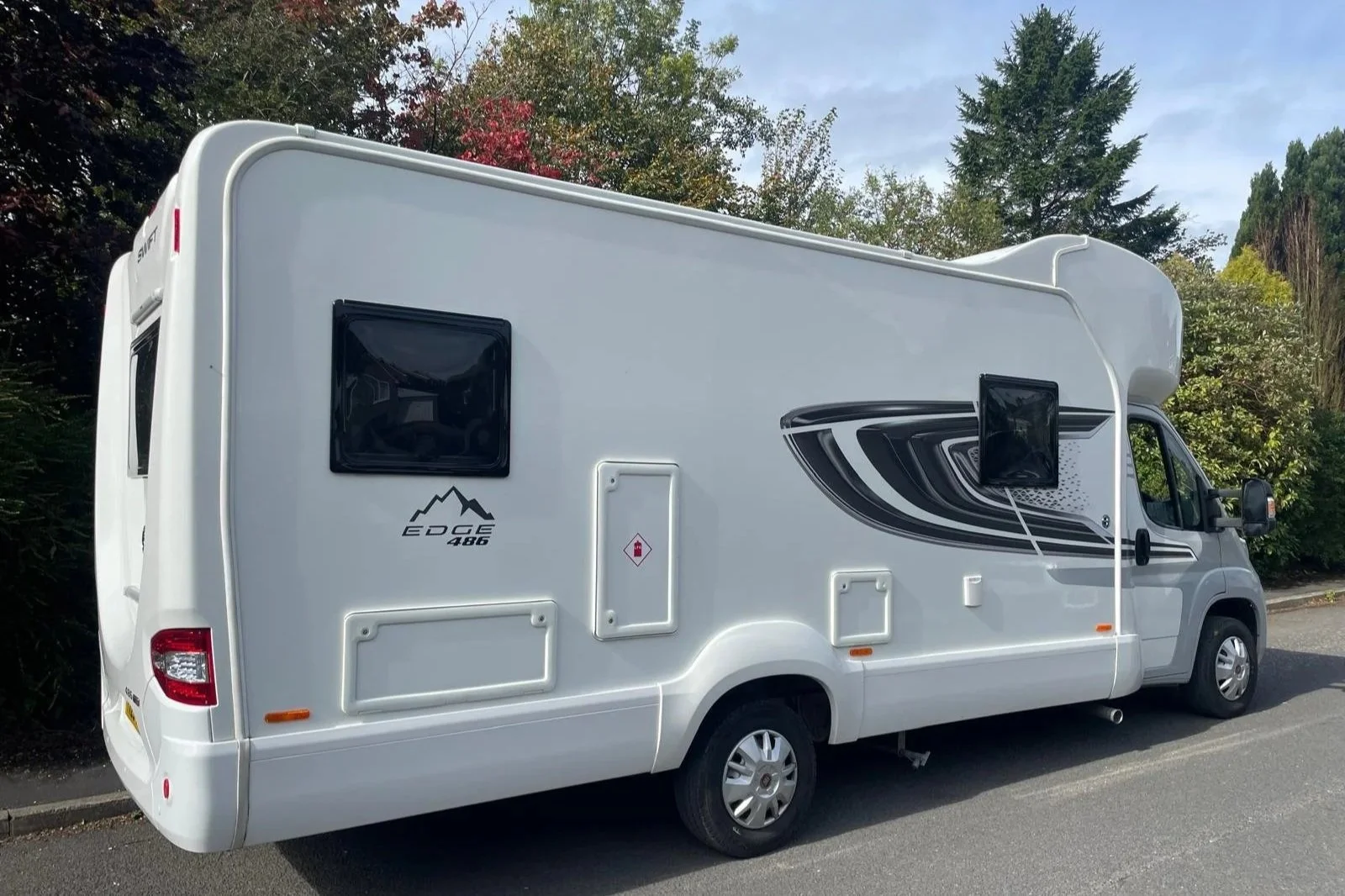 White recreational vehicle with black graphic decals parked on the street near trees.