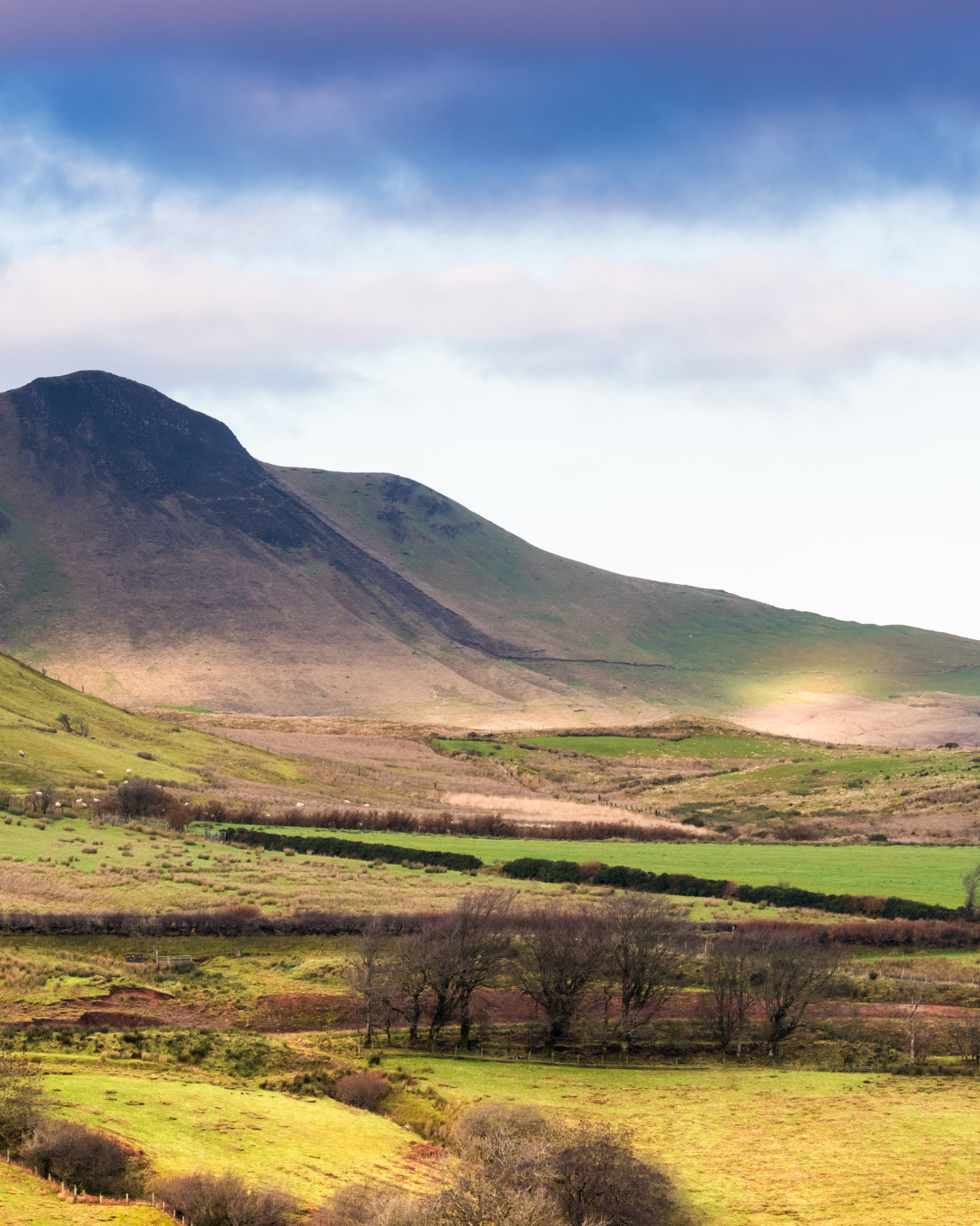 Landscape of rolling green hills and mountains under a partly cloudy sky.