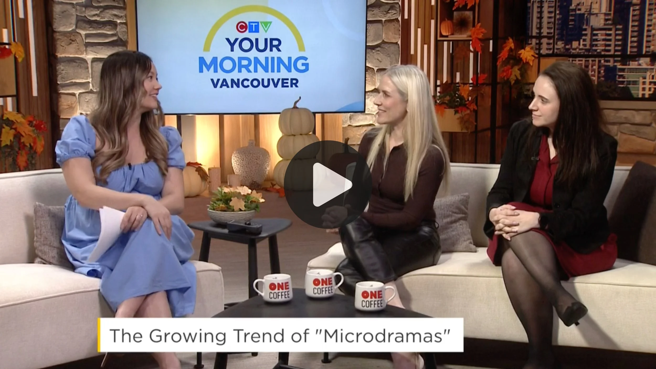Three women sitting on a couch during a TV interview on 'Your Morning Vancouver' show. The background features autumn decorations including pumpkins and fall leaves. There is a small table with three coffee mugs that say 'ONE COFFEE' and a TV screen displaying the show's logo.