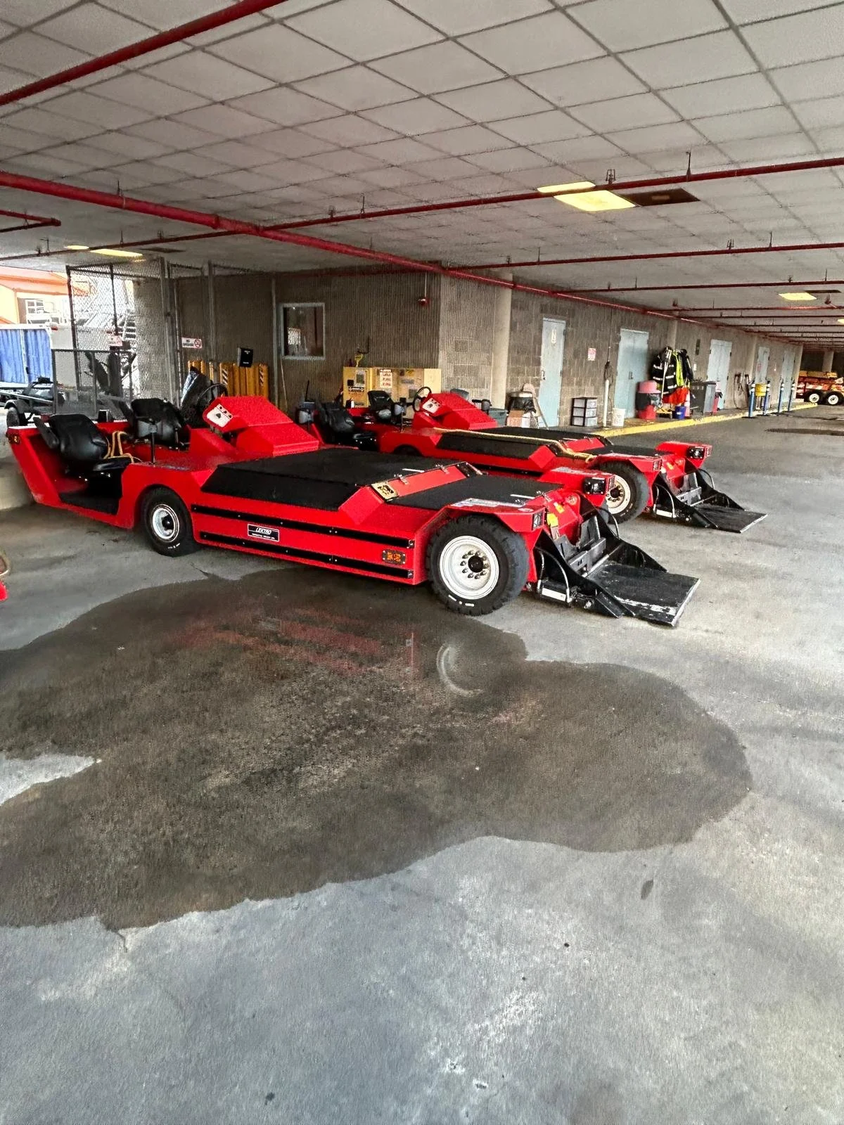 Multiple red fire-type vehicles with treads, parked inside a parking garage.
