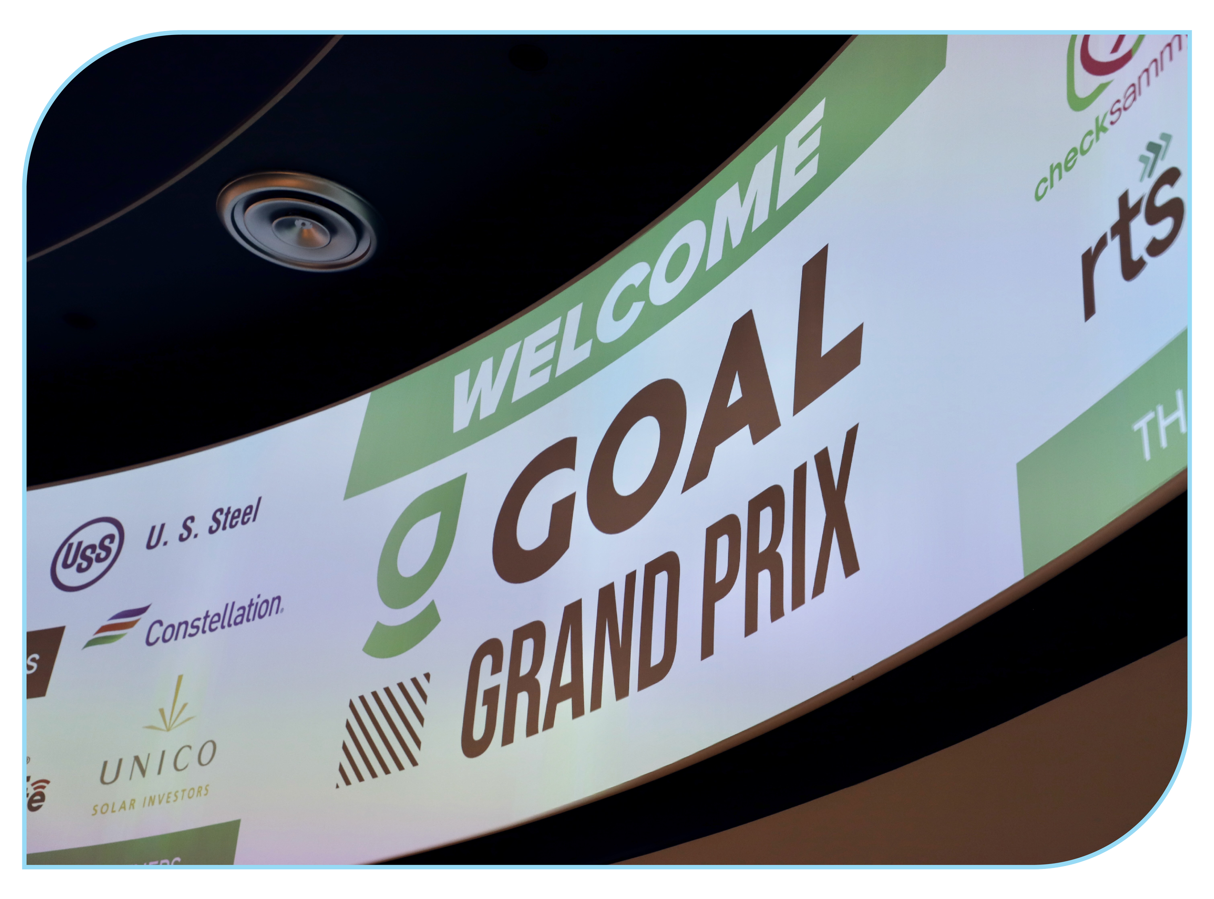 A large indoor digital display with the text "Welcome to GOAL Grand Prix" and various sponsor logos including U.S. Steel, Constellation, and Unico Solar Investors.