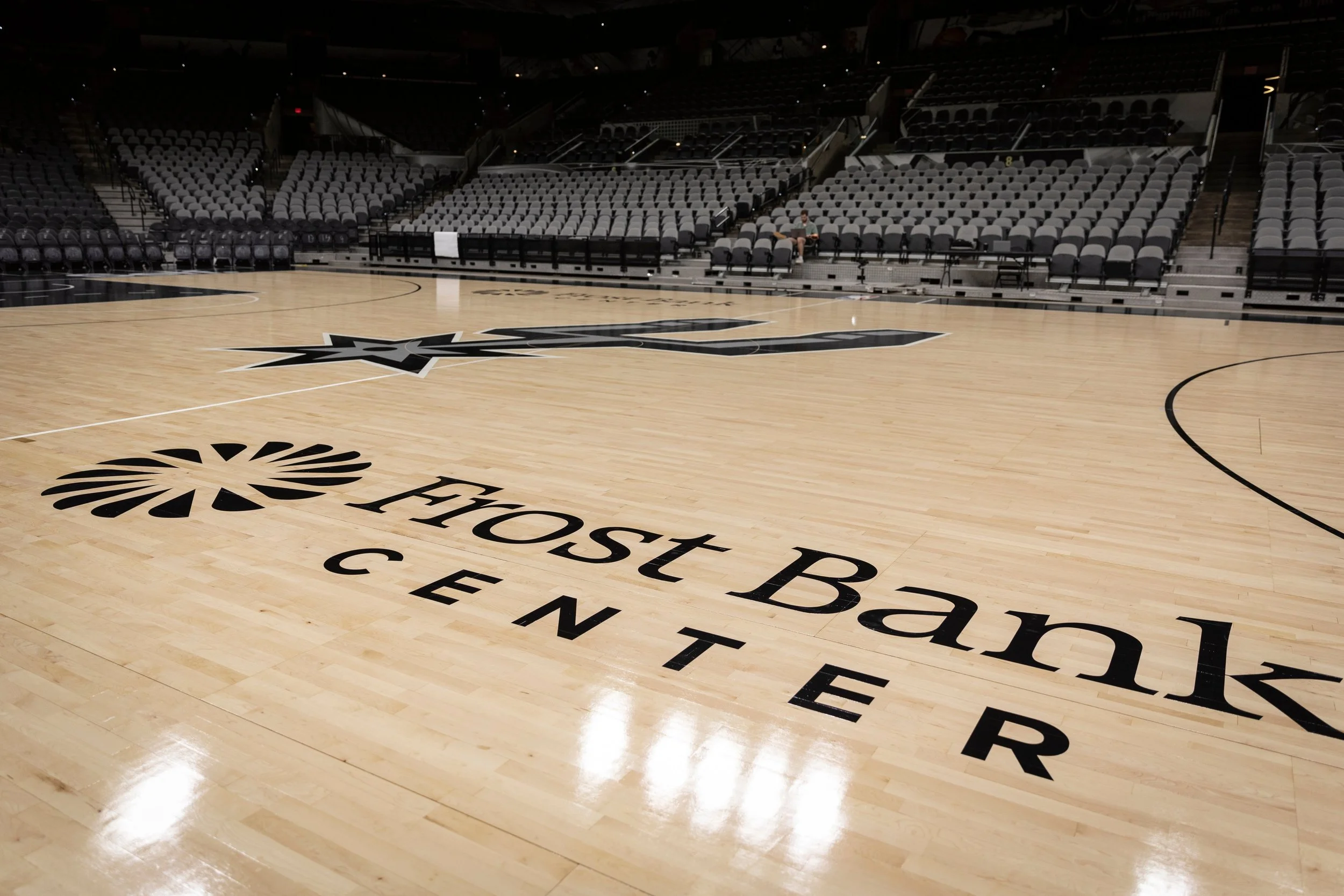 Empty basketball court at the Fost Bank Center, with the team logo on the polished wooden floor and rows of gray seats surrounding the court.
