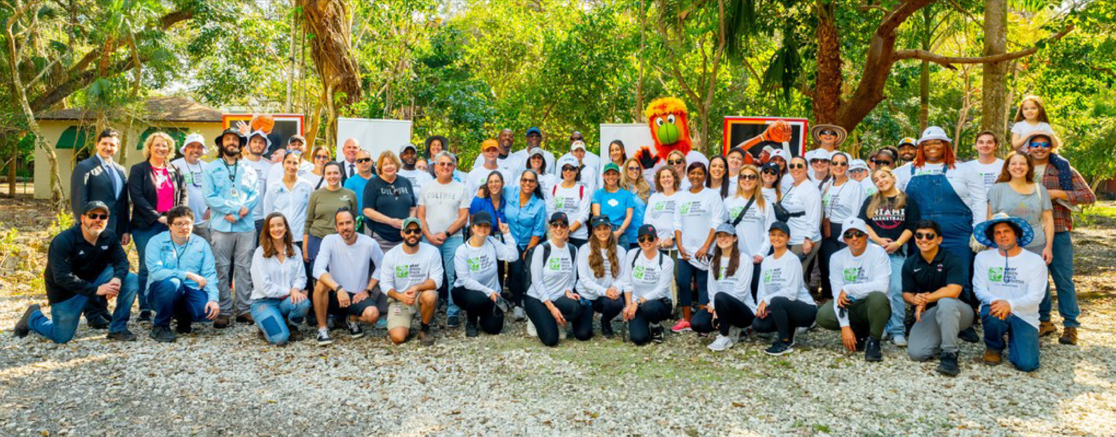 Group of people outdoors in a park with trees, some are standing and others kneeling, smiling at the camera.
