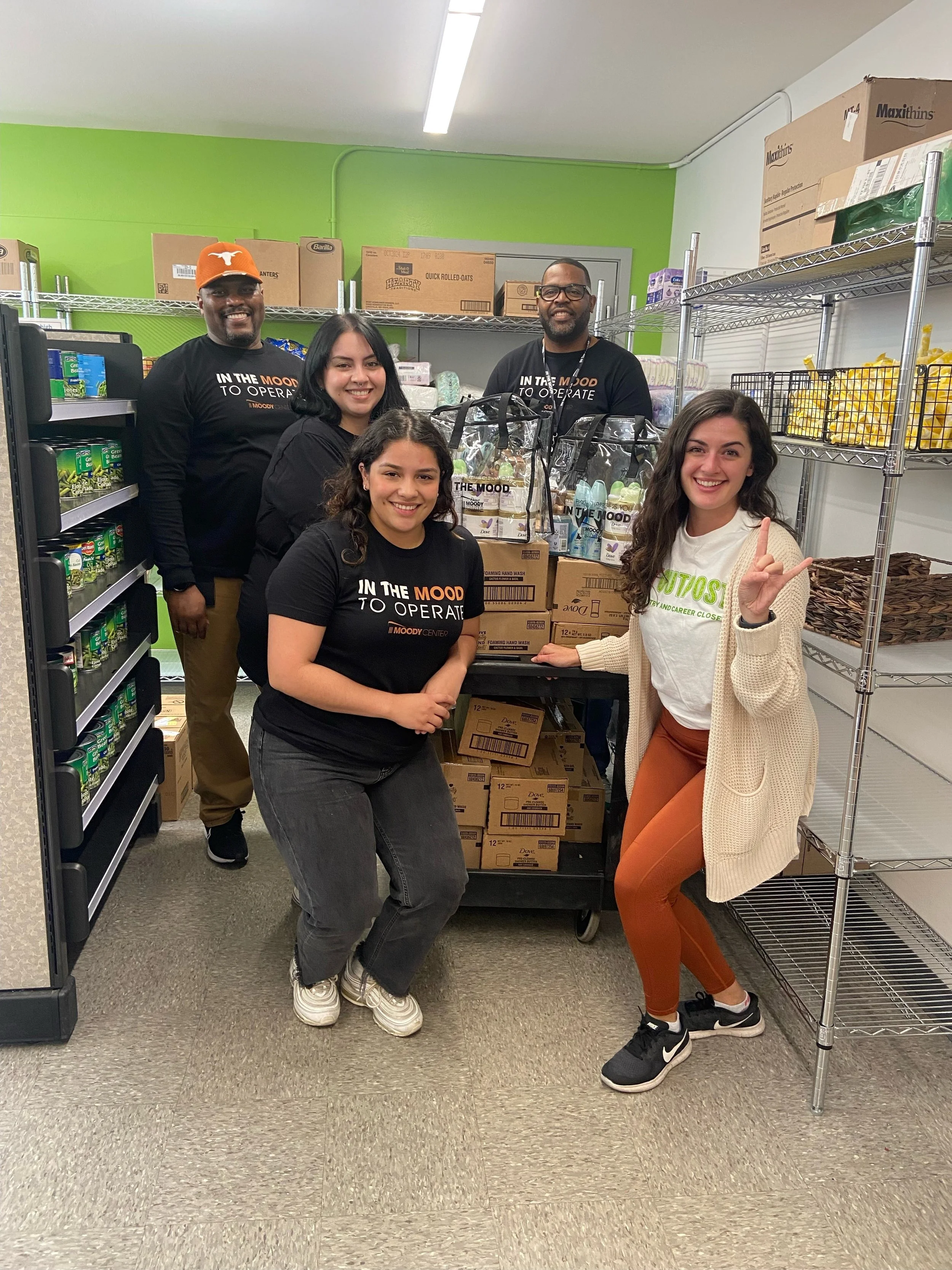 Group of five people standing in a room with shelves and boxes, smiling for the camera.
