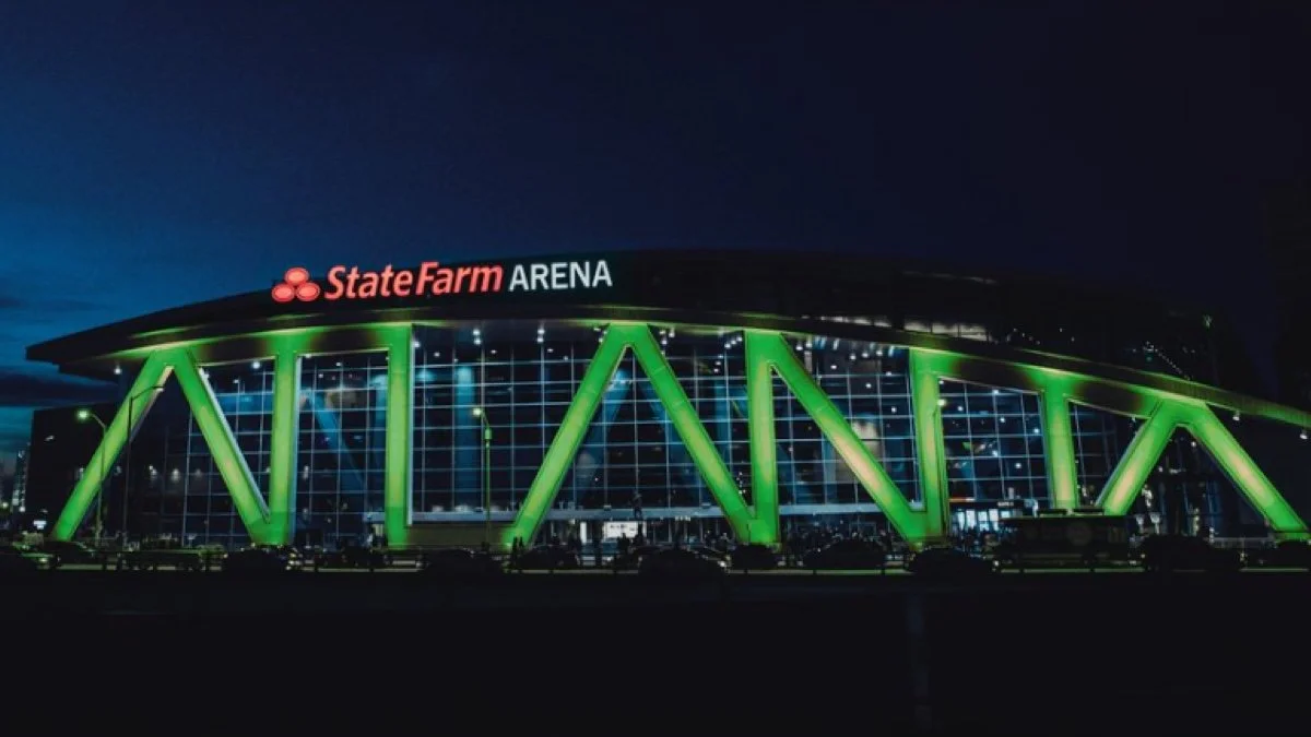 Night view of State Farm Arena with illuminated green structural beams and a glass facade.