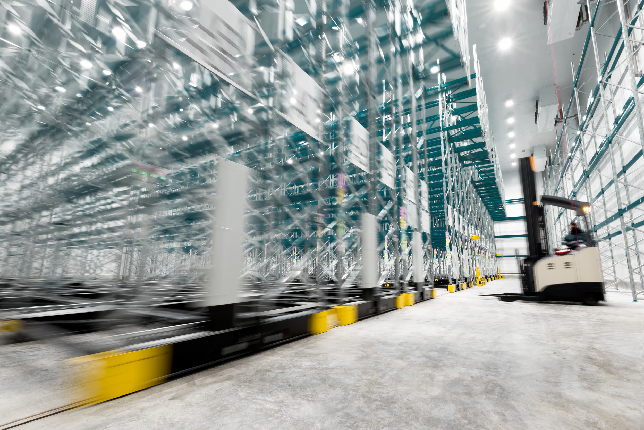 Warehouse worker operating a forklift among tall storage racks filled with items, with some motion blur indicating movement.