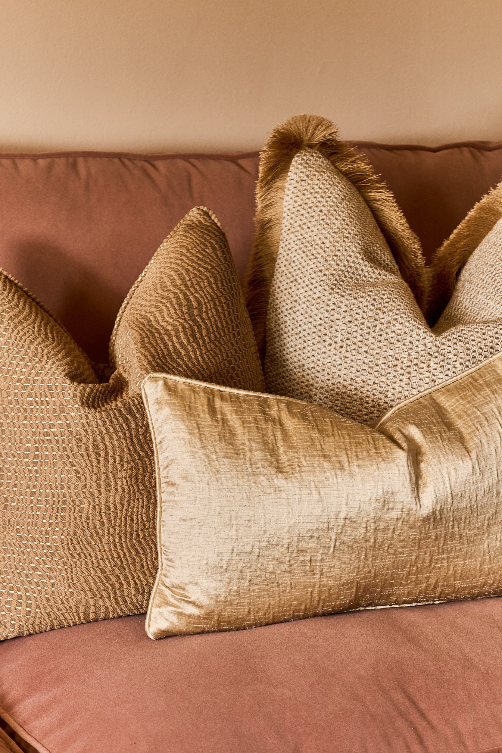 A collection of beige decorative pillows with various textured patterns on a pink couch.