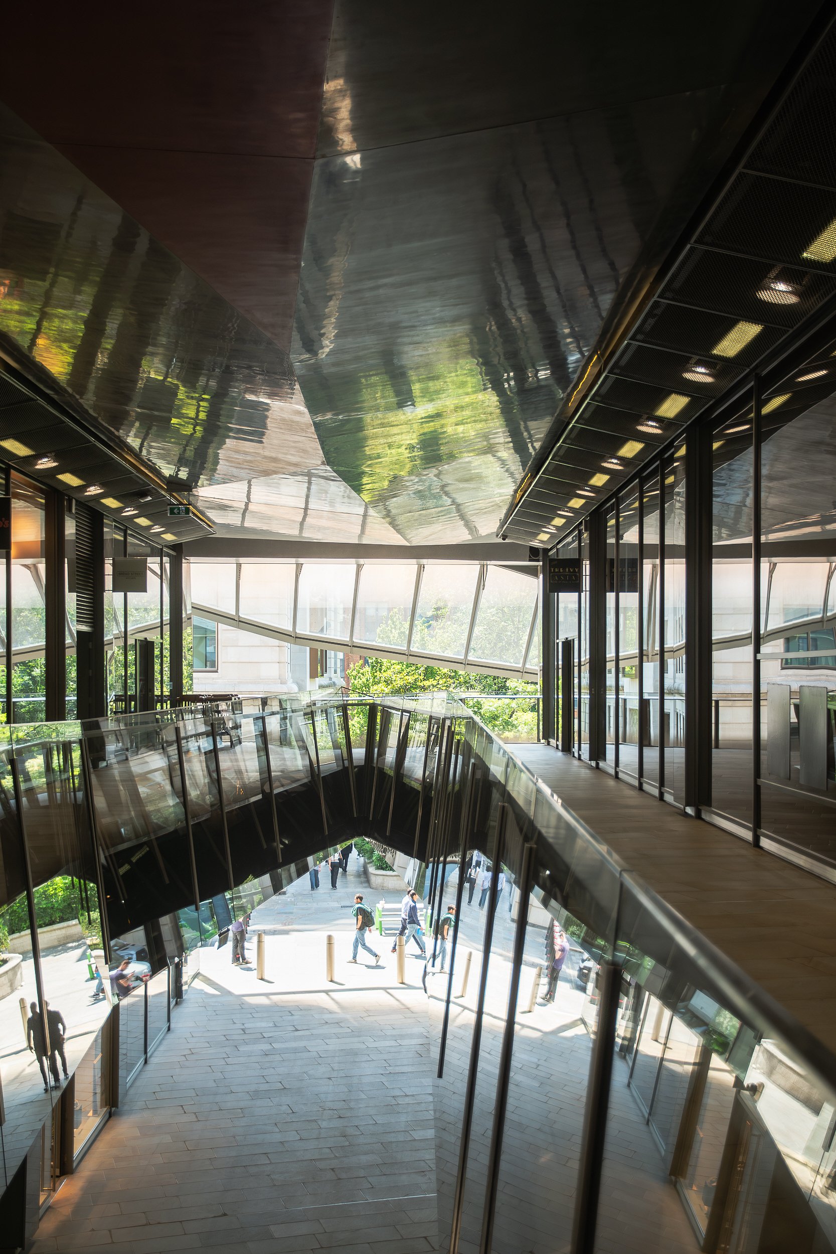 Modern building interior with glass walls and stairs, view of pedestrians outside.