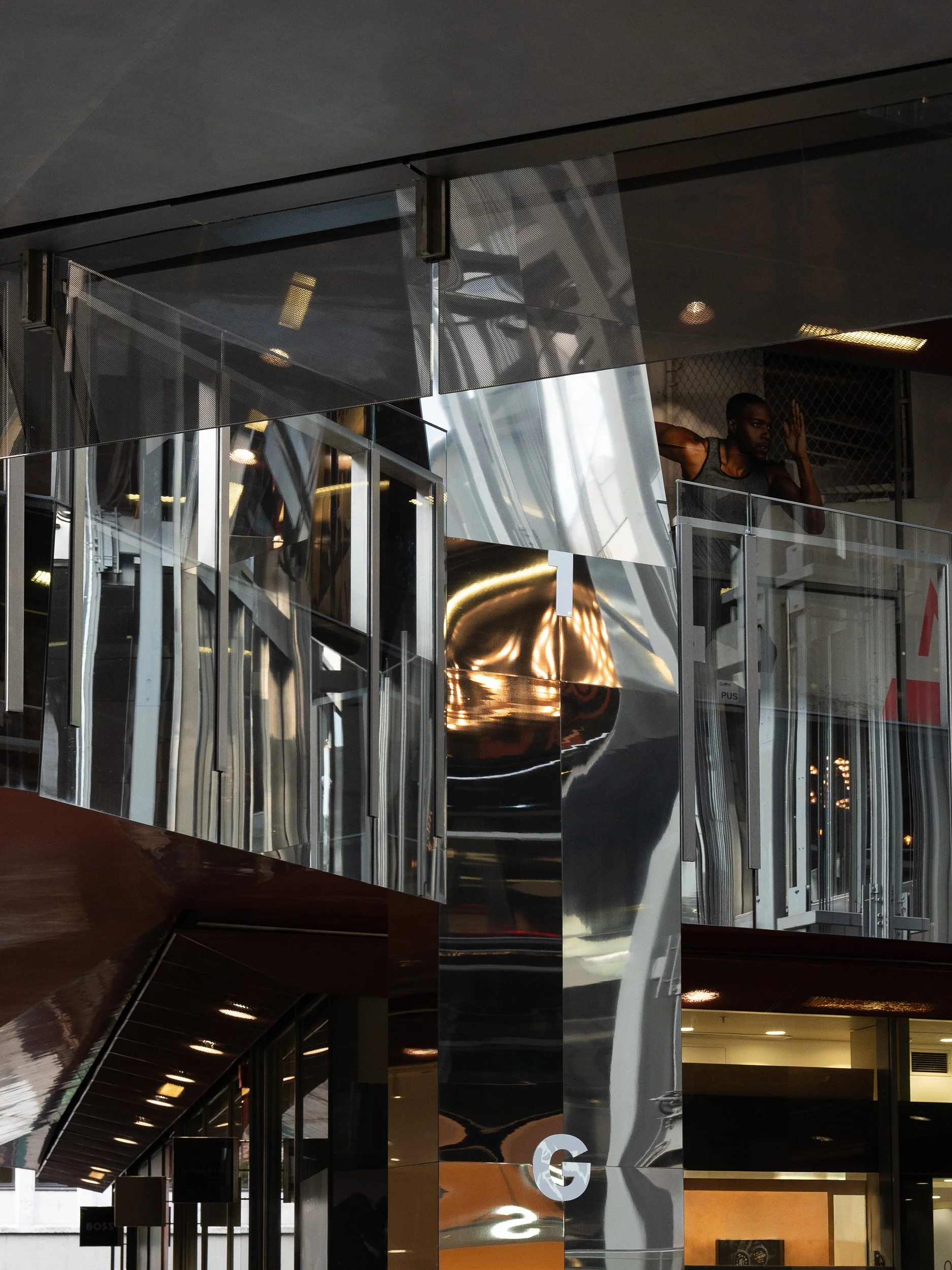 Modern building with reflective metallic surfaces and glass, featuring people on an upper balcony and interior lighting.