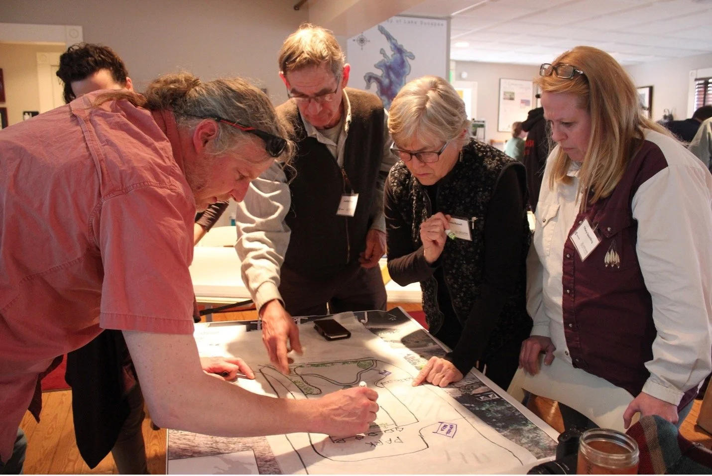 People gather around a diagram on a table, drawing on the diagram and working