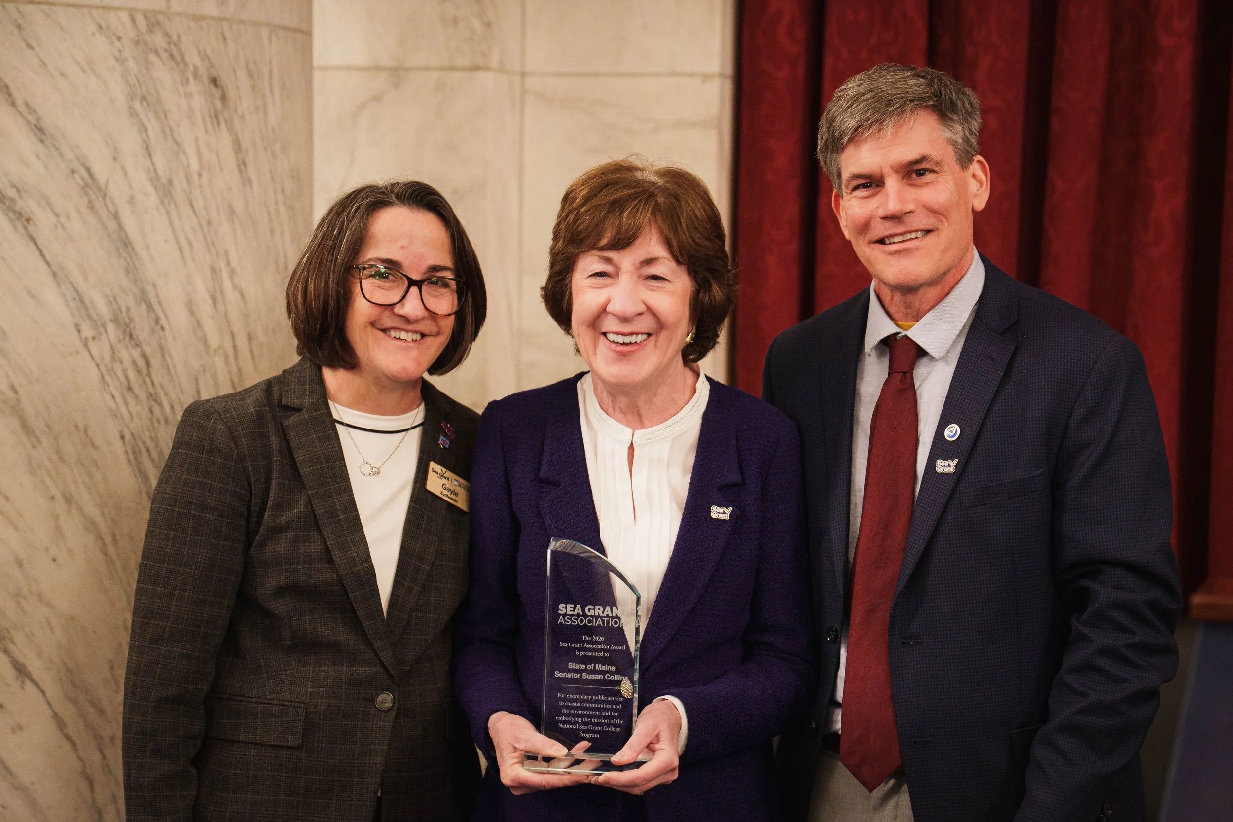 Senator Susan Collins stands with her Sea Grant Association Award, alongside Gayle Zydlewski and Erik Chapman.