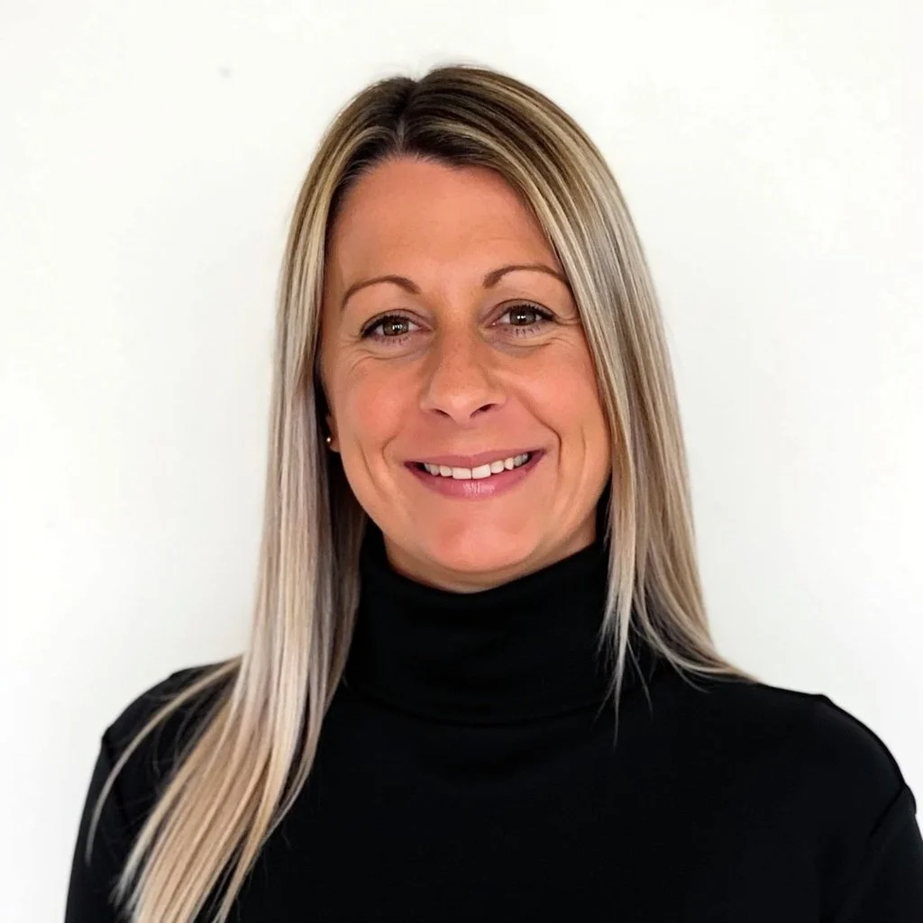 A woman with long blonde hair wearing a black turtleneck, smiling, with a plain white background.